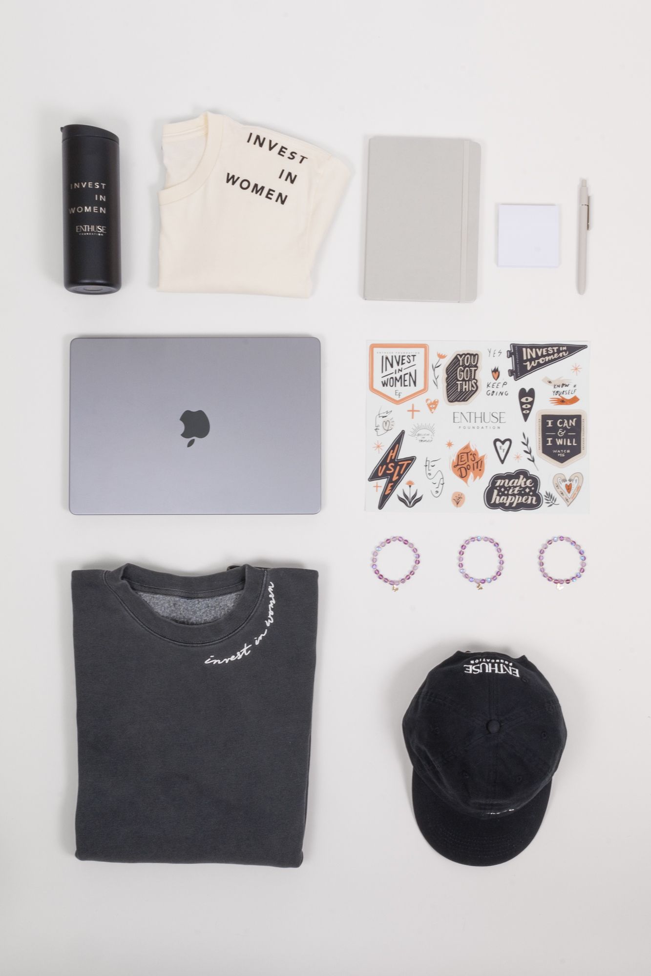 Organized layout of laptop, apparel, stickers and accessories on white background.