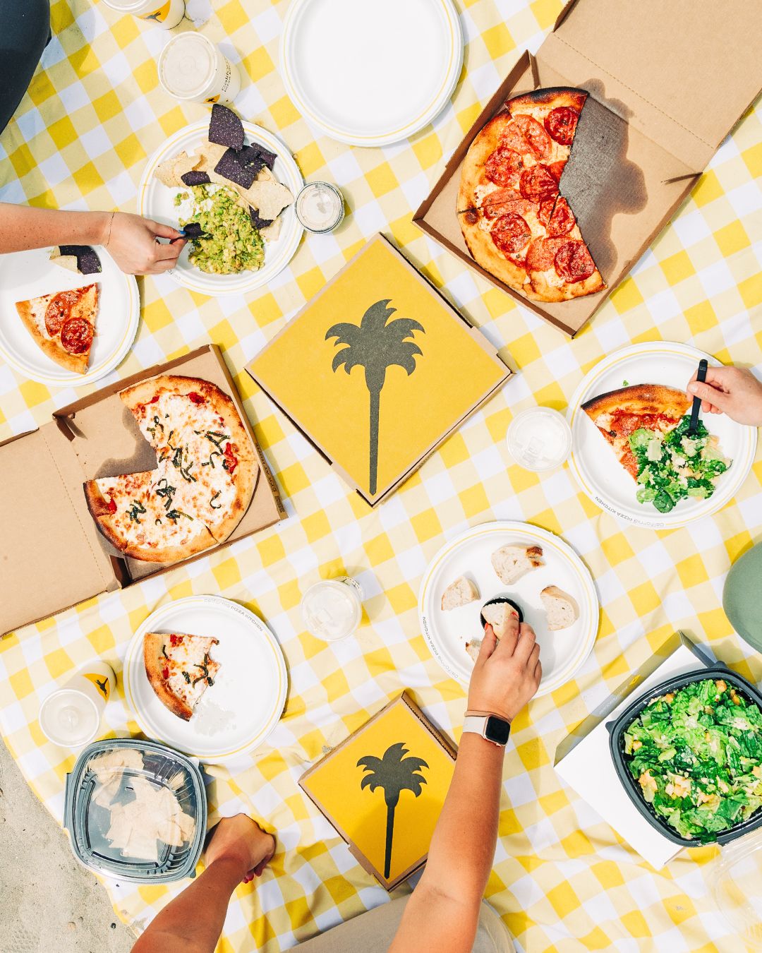 Overhead view of pizza and salad on yellow checkered tablecloth with palm tree decorations.
