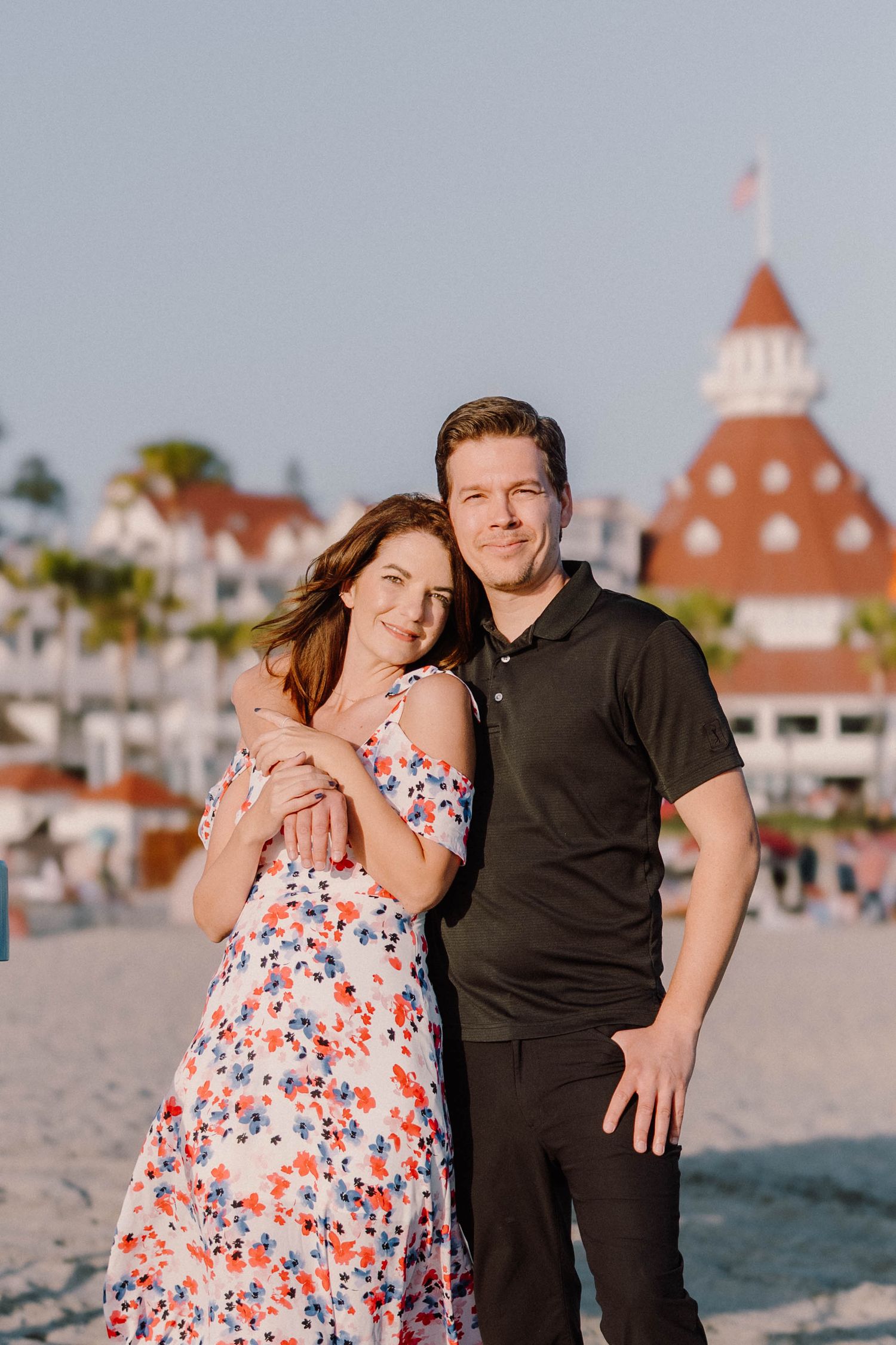 Couple poses on beach with historic Hotel del Coronado building in background.