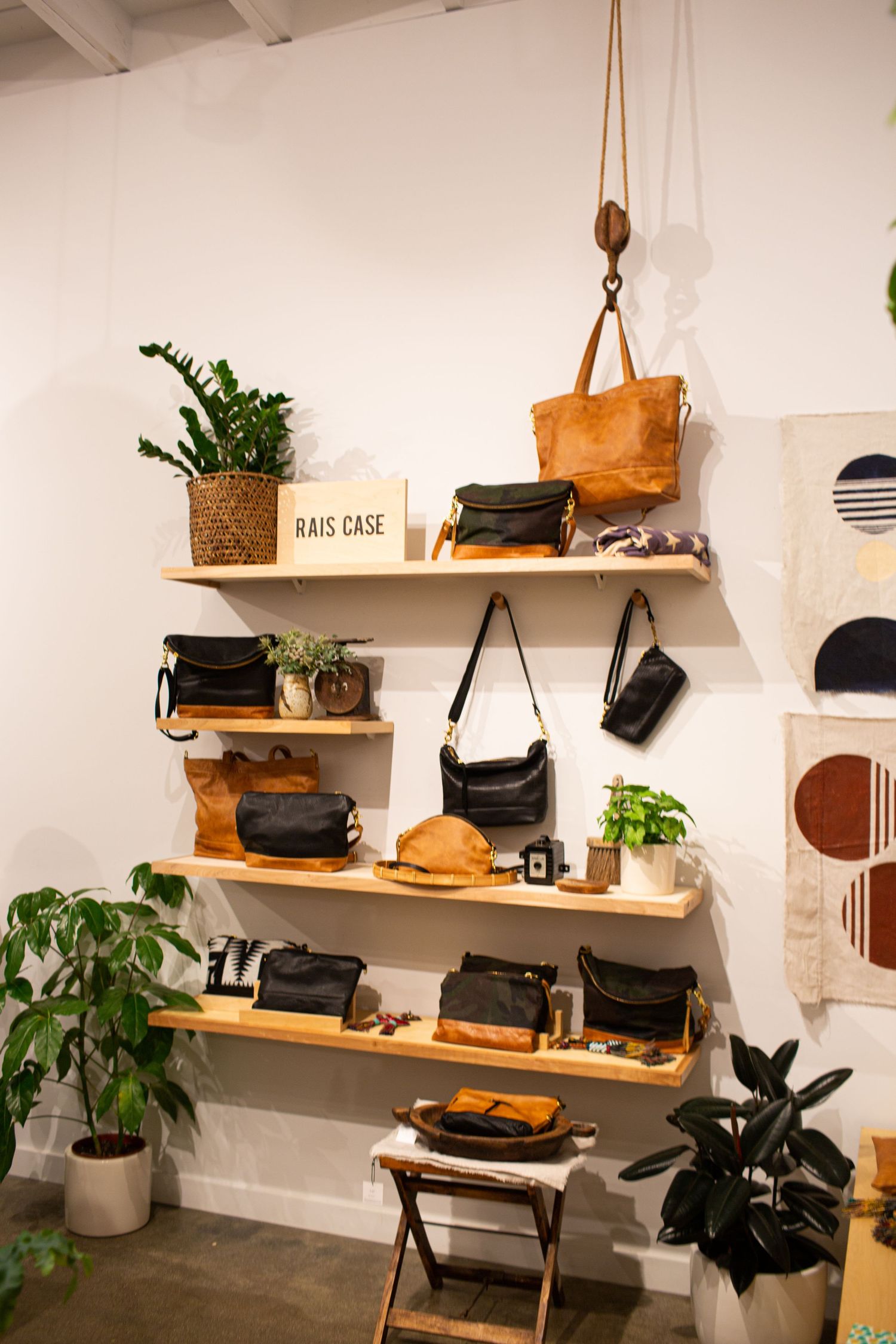 Modern retail display with wooden floating shelves showcasing leather bags, accessories and potted plants against white walls.