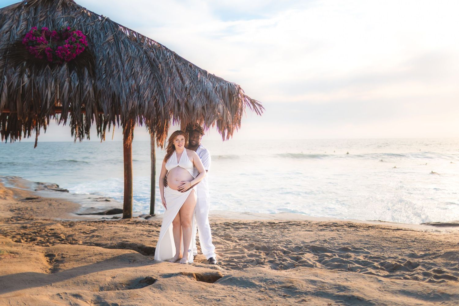 A romantic beachside wedding photoshoot featuring a couple in white attire against a scenic coastal backdrop at sunset.