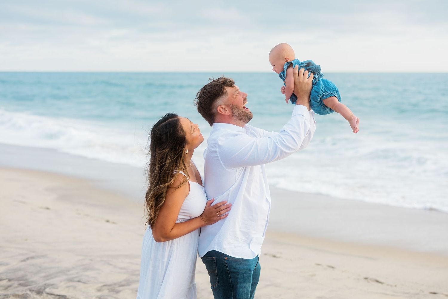 A tender family moment captured on a peaceful beach with ocean waves in the background.