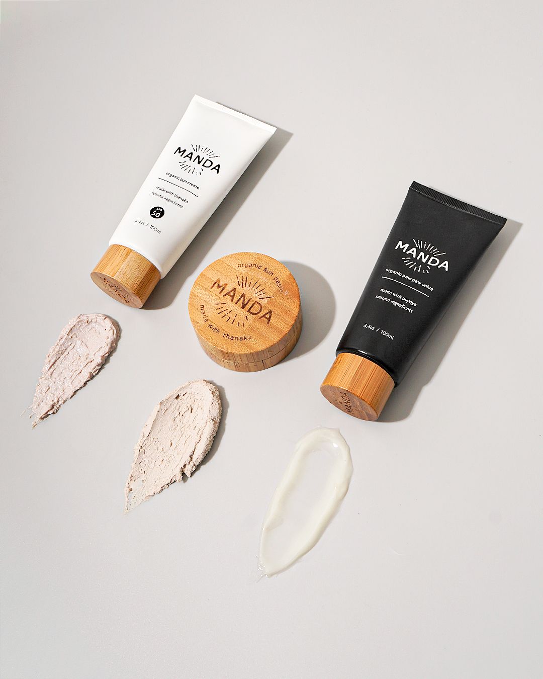 Manda skincare products with cream texture swatches displayed on white background.