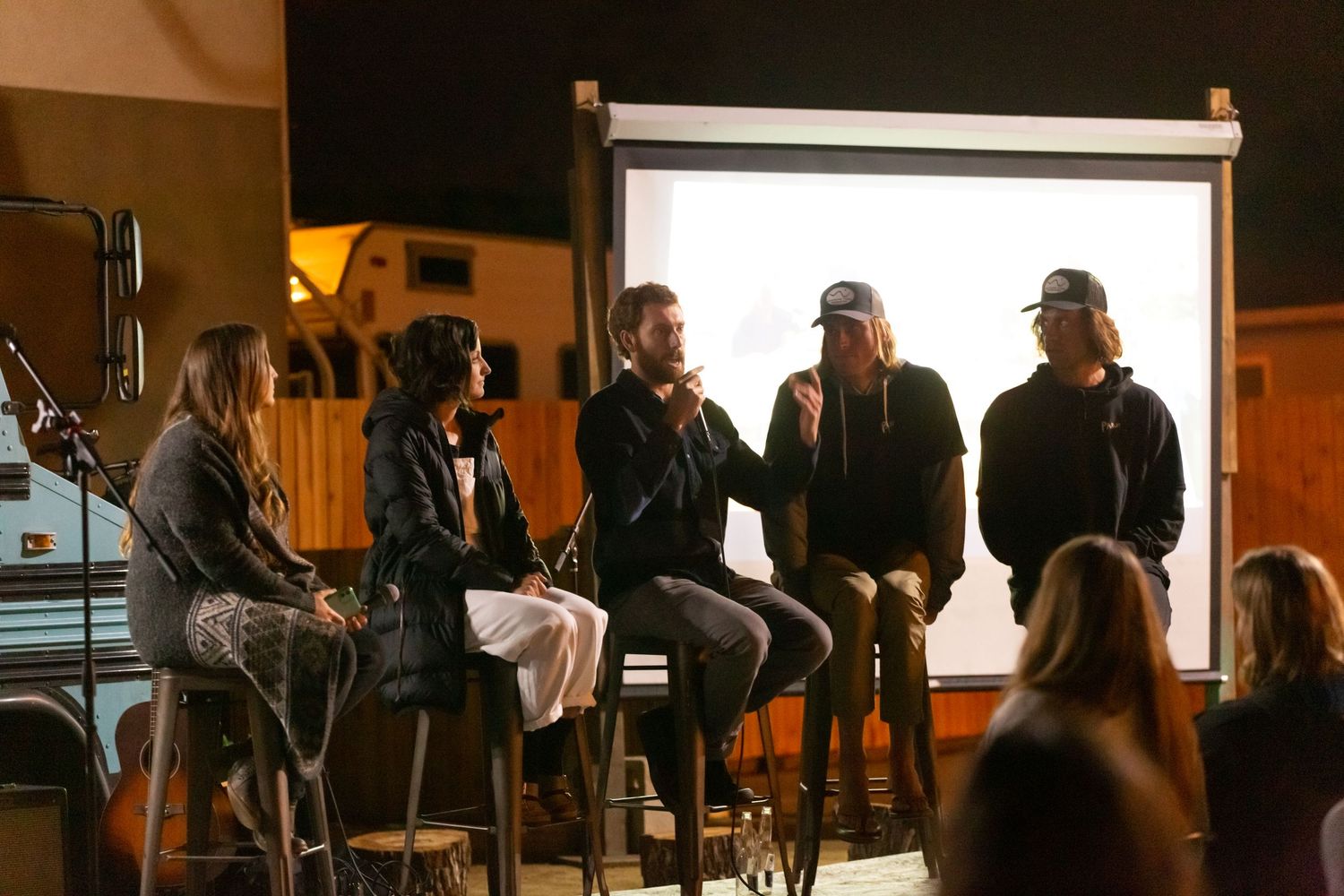 People gather in a dimly lit room with projected presentation screen visible in the background.