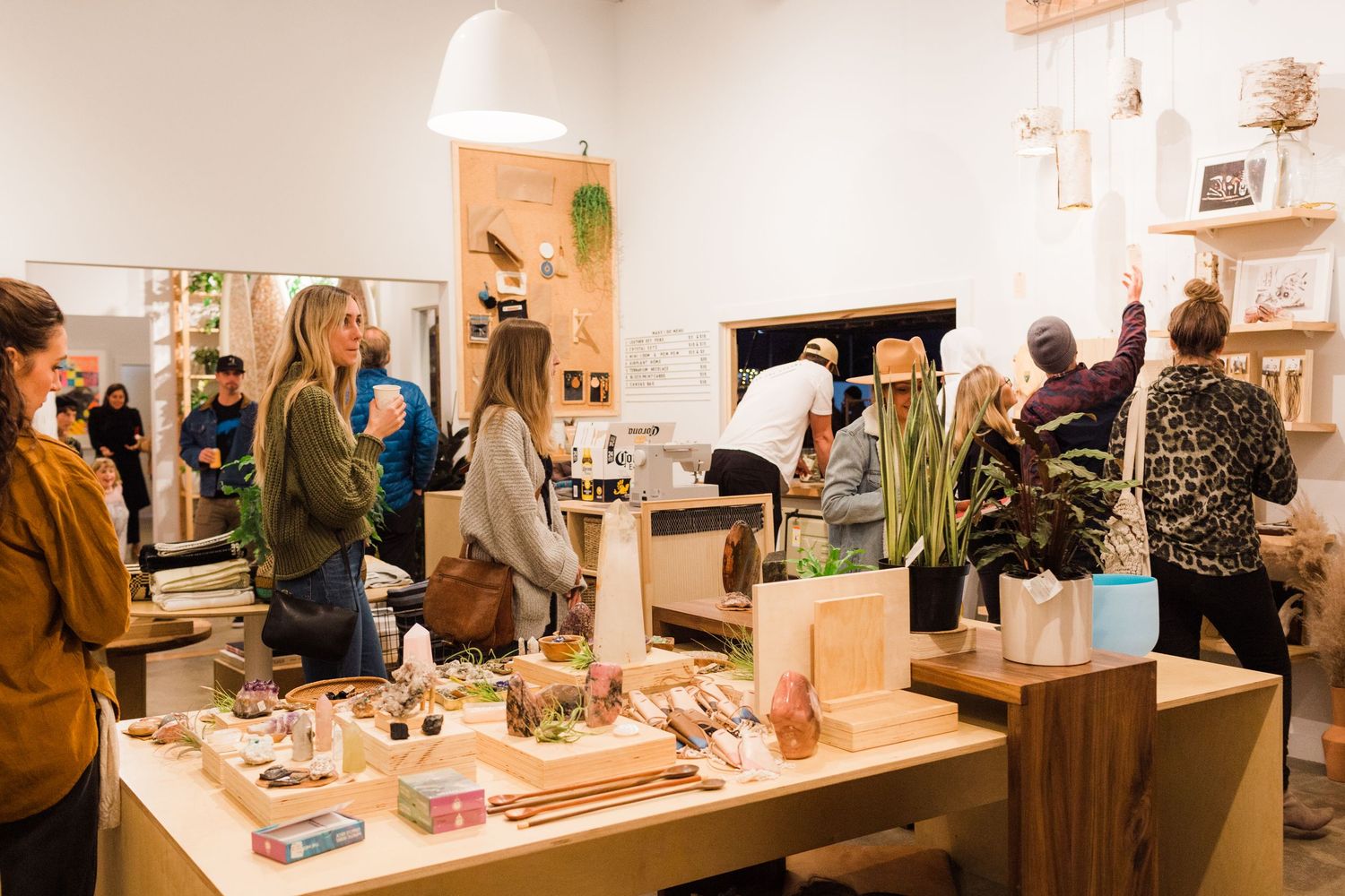 Customers browse products at a cozy artisan market featuring handmade goods and local merchandise displayed on white tables.