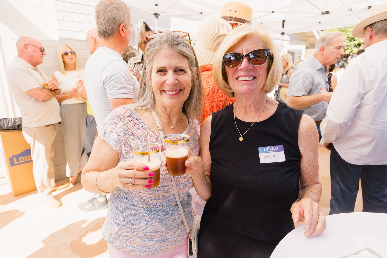 Guests socializing and holding drinks at a casual outdoor party under a white tent.