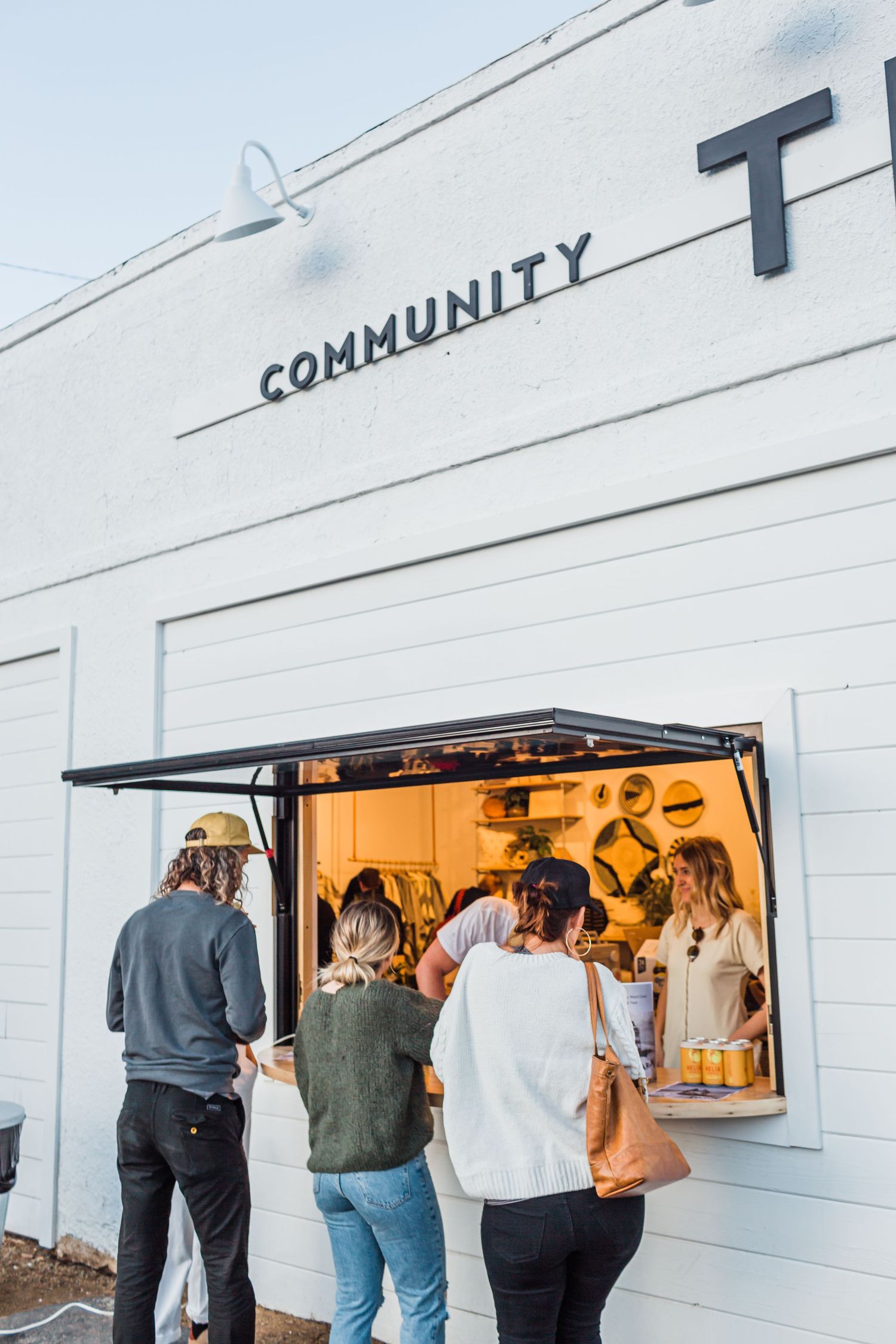 People gathered around outdoor service windows of a white building with Community signage above.
