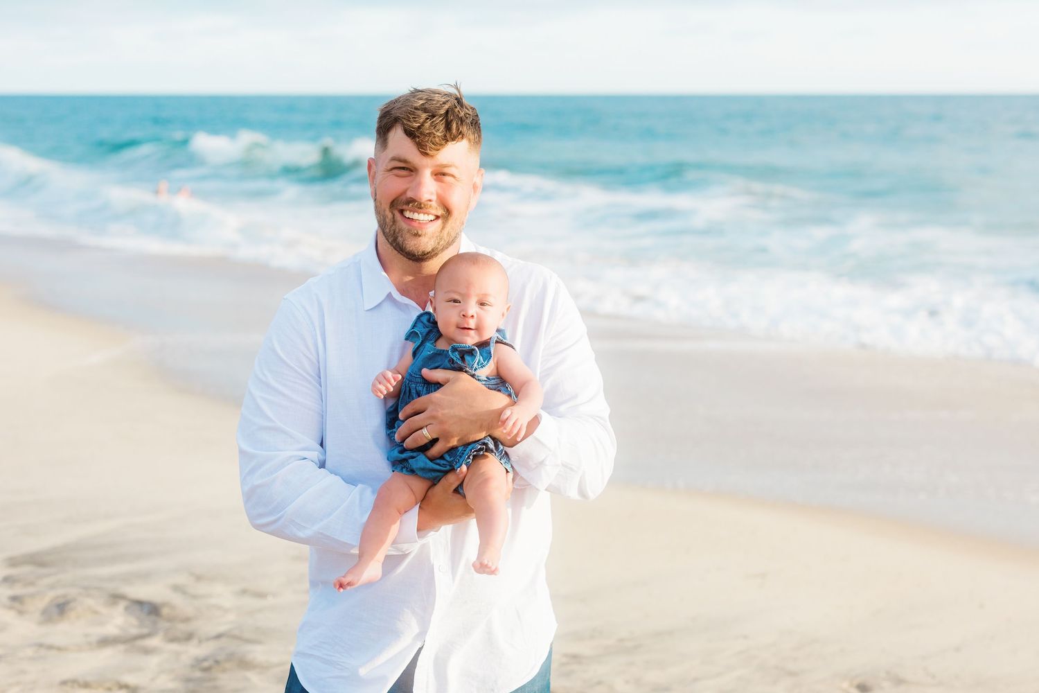 A heartwarming beach portrait with a small baby in blue against ocean waves.