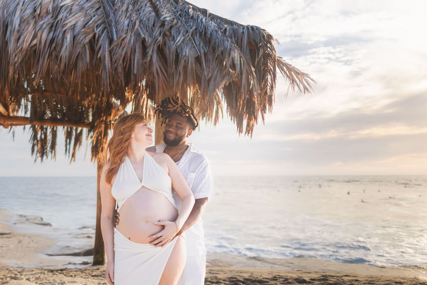 Romantic beach photoshoot with palm frond umbrellas and gentle waves at golden hour.