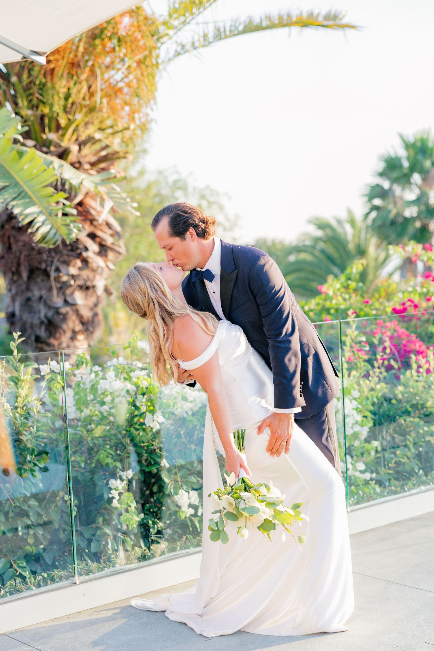 Wedding couple shares joyful moments together on an outdoor terrace surrounded by tropical plants.