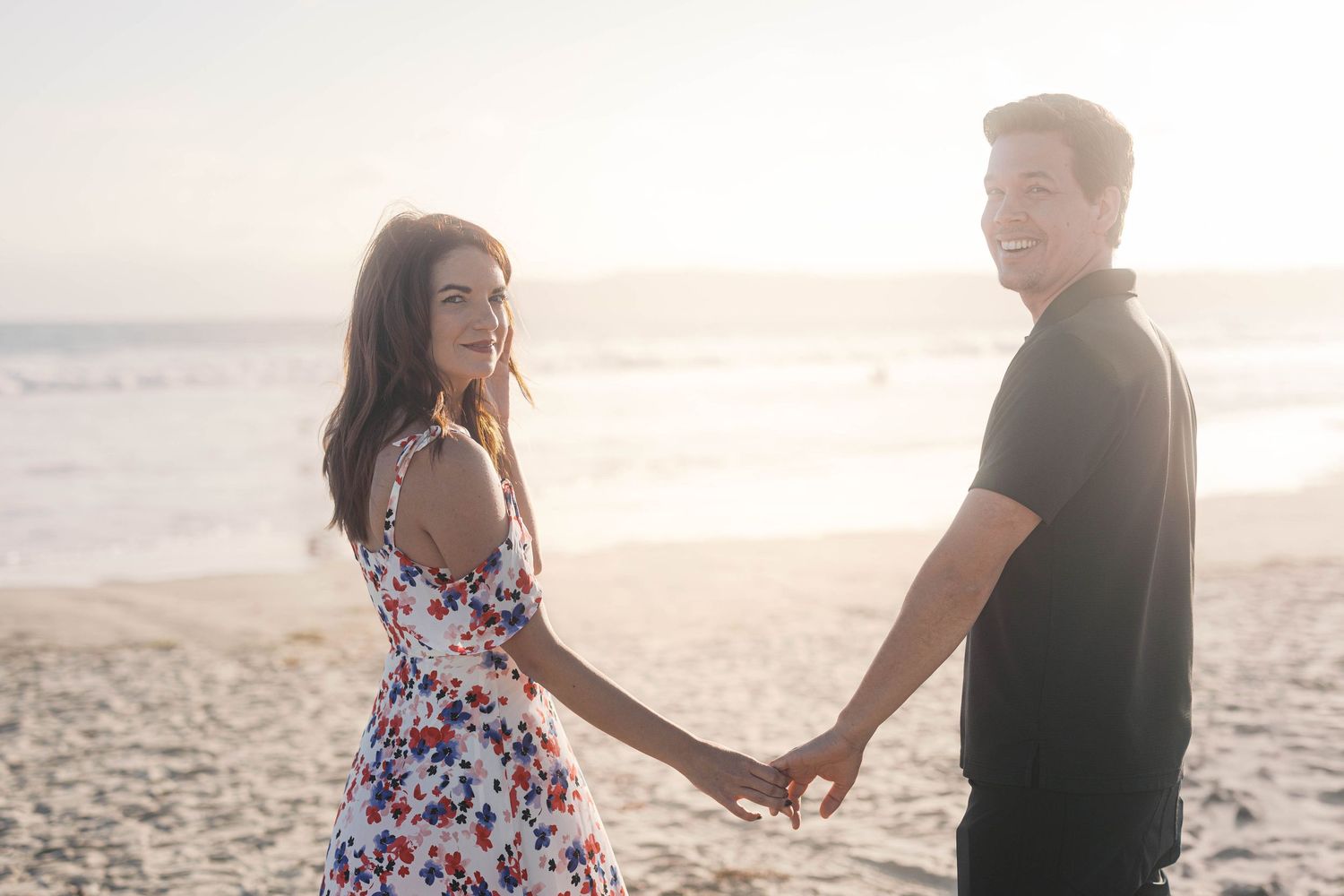 Couple in casual attire enjoying romantic moment on sandy beach at sunset.