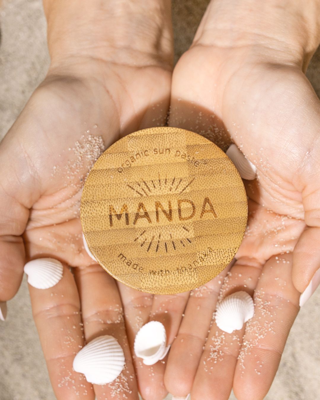 Manda wooden applicator with sunscreen product demonstrated in hands with white cream.
