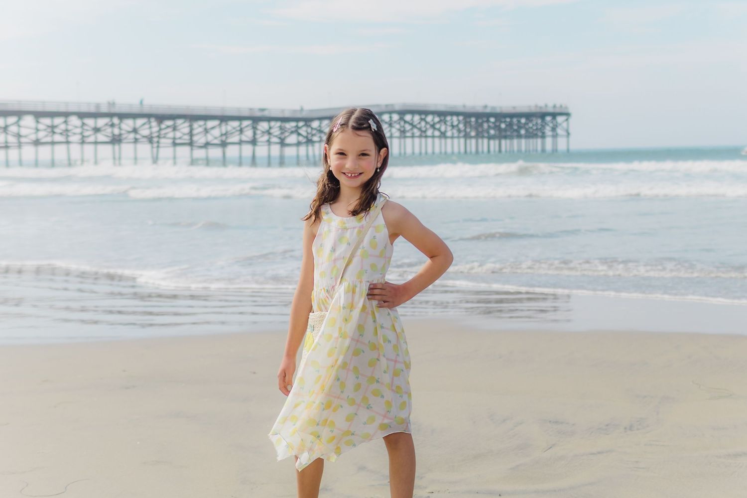 Child playing and running on beach near pier with waves crashing in background.