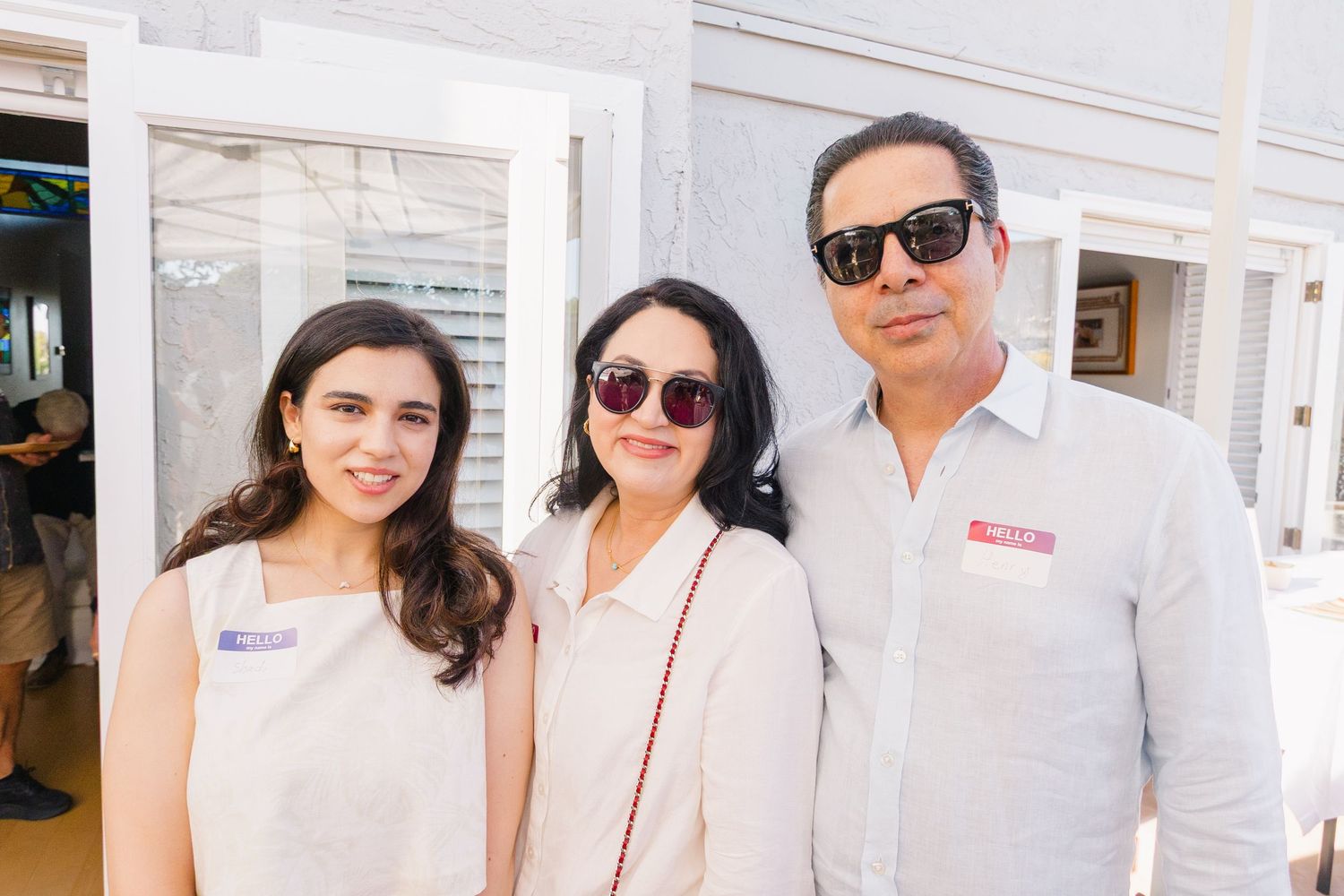 Guests in summer attire gathering outside a white building during a daytime event.