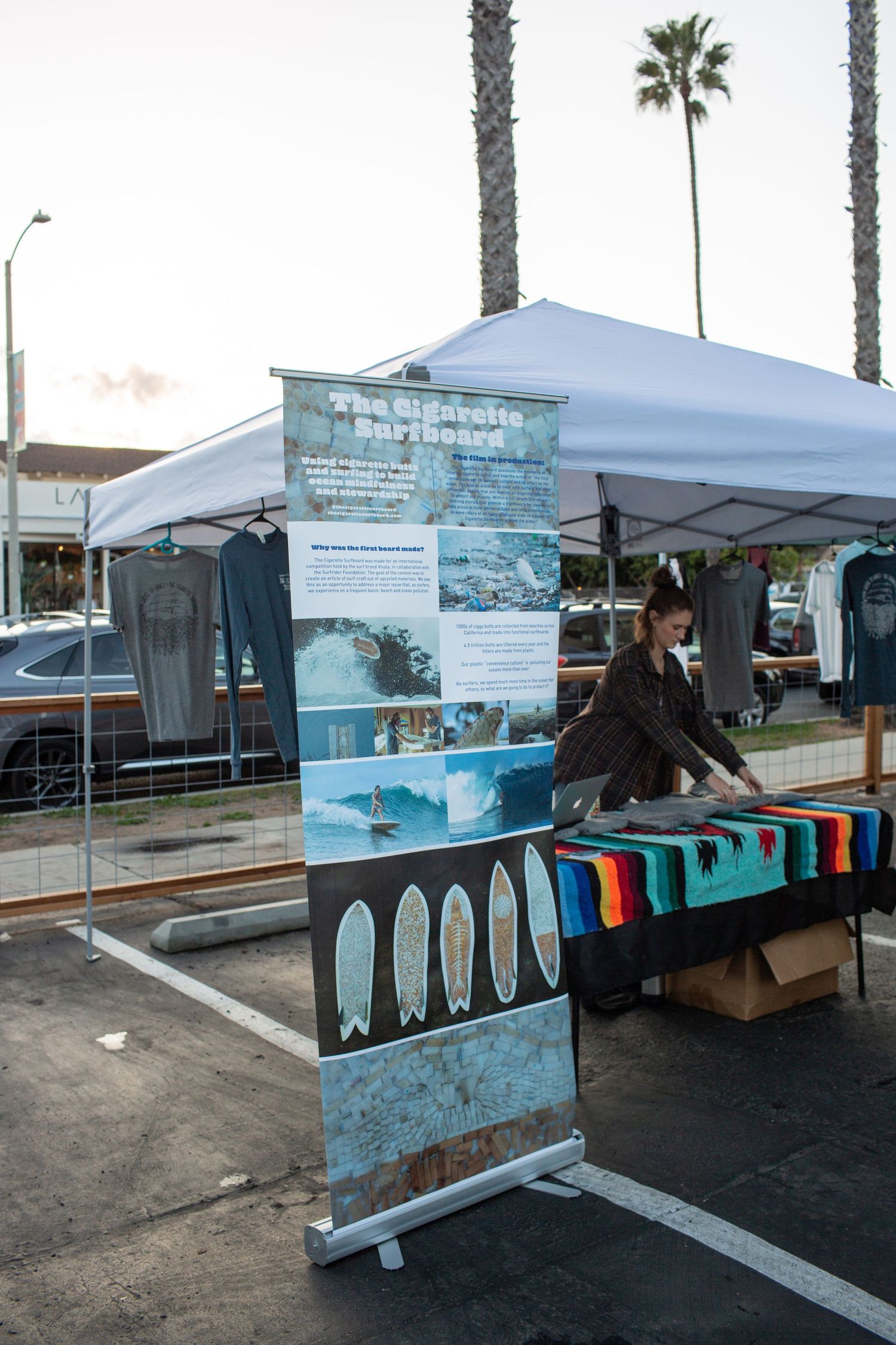 Outdoor market booth setup with informational display banners and merchandise tables under white canopy tents.