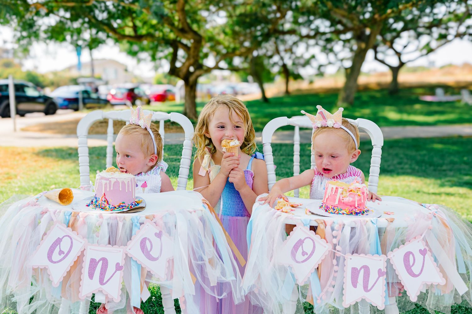 Pink and purple birthday party decorations with a 'One' banner strung between trees.