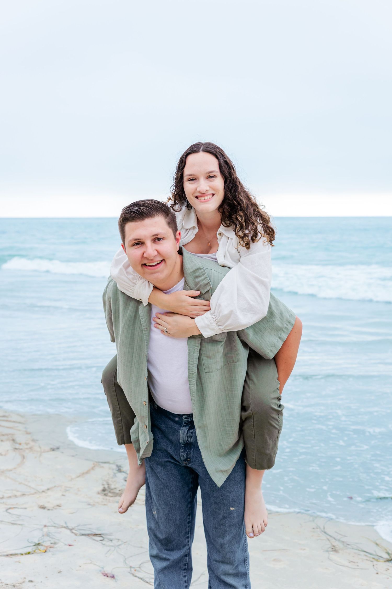 A piggyback pose creates a sweet moment between a couple on a scenic beach.