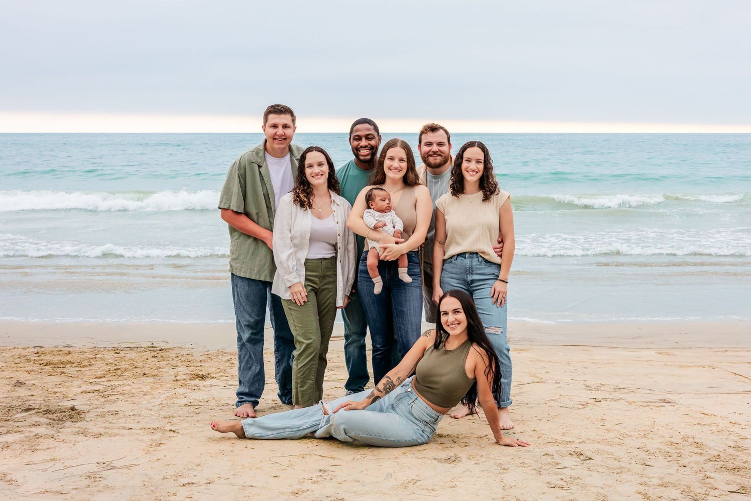 Extended family poses together on a sunny beach with ocean waves in the background.