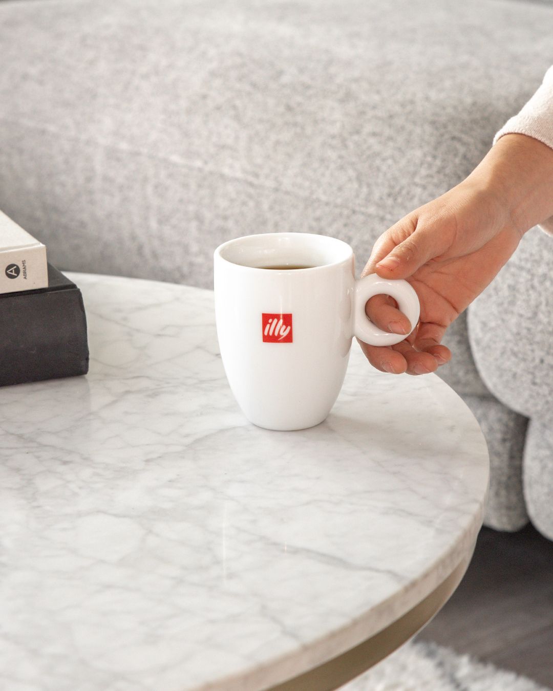 White illy espresso cup being placed on light marble table surface.