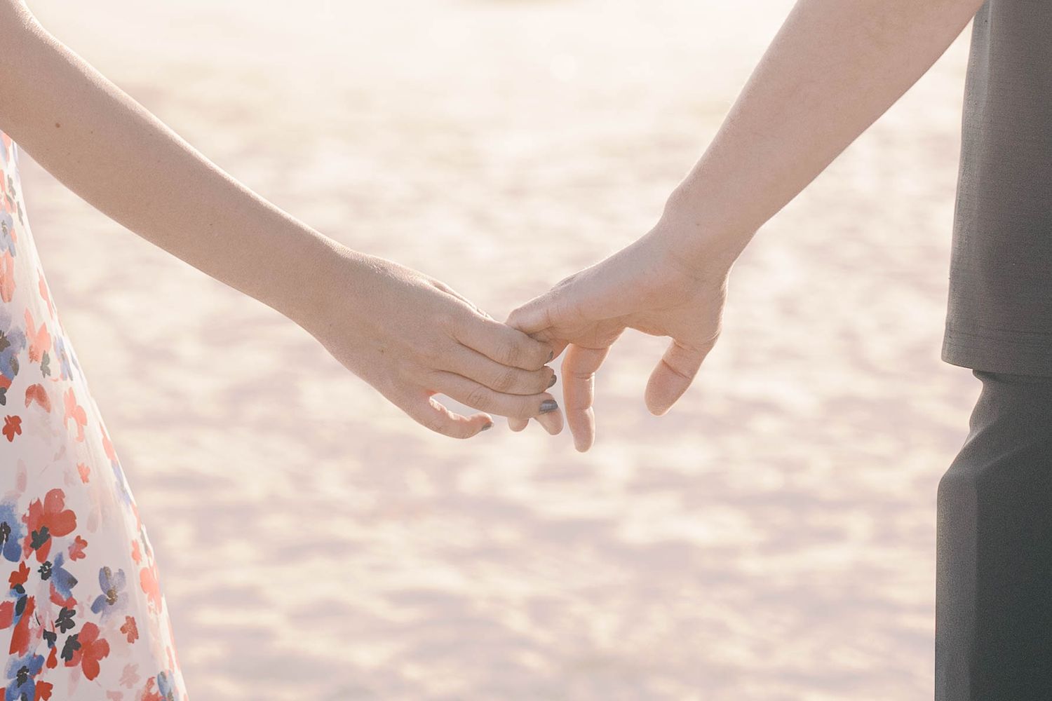Close up of couple's hands joined together walking on beach at sunset.