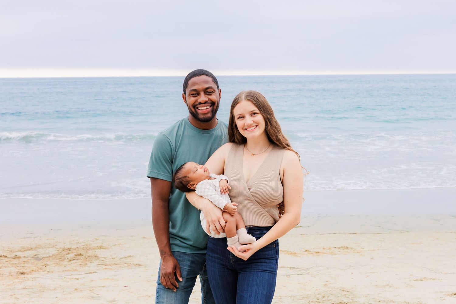 A family of three poses for a portrait on a sunny beach.