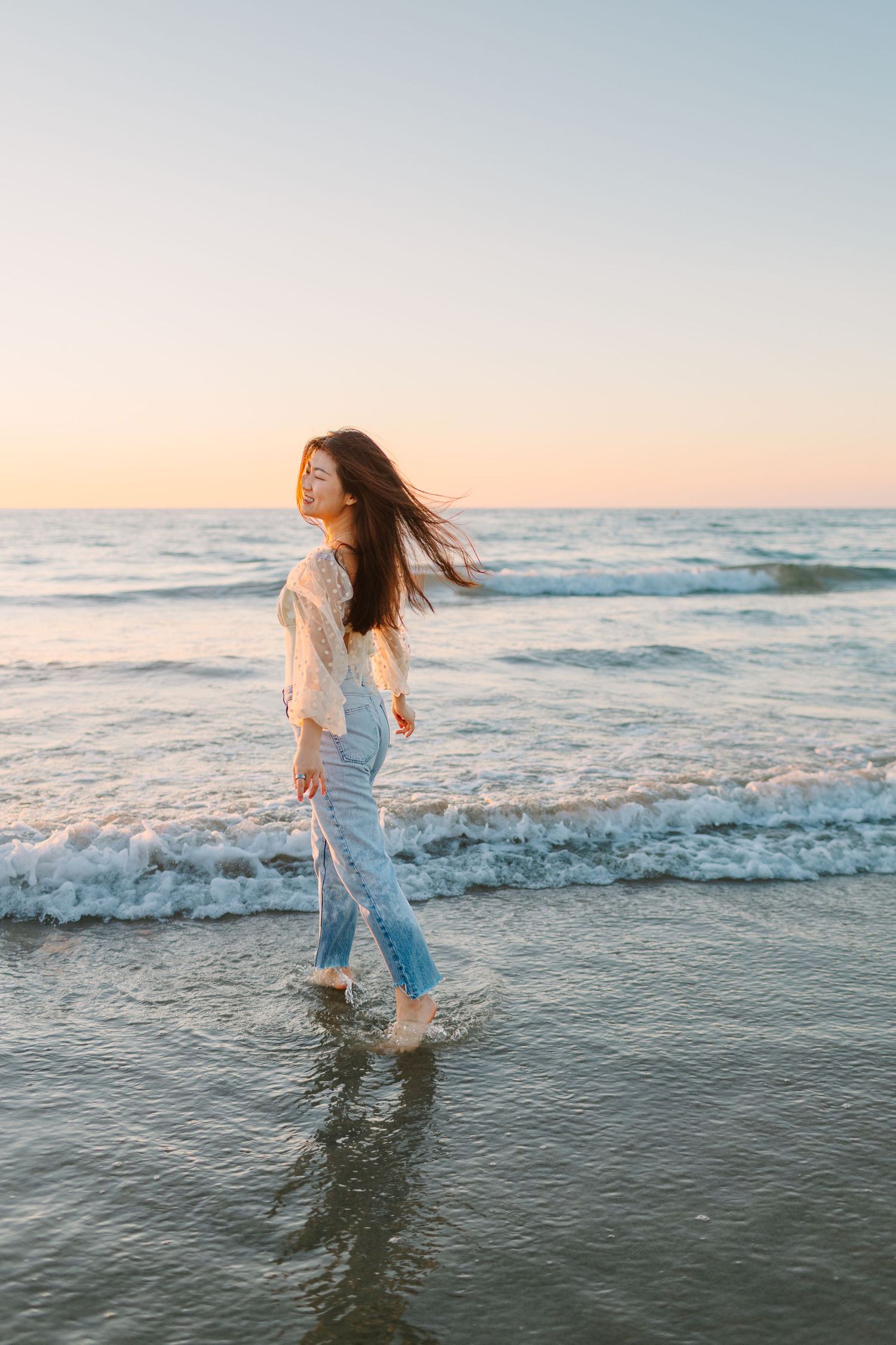 Woman in white top and jeans plays in ocean waves during golden hour photoshoot.