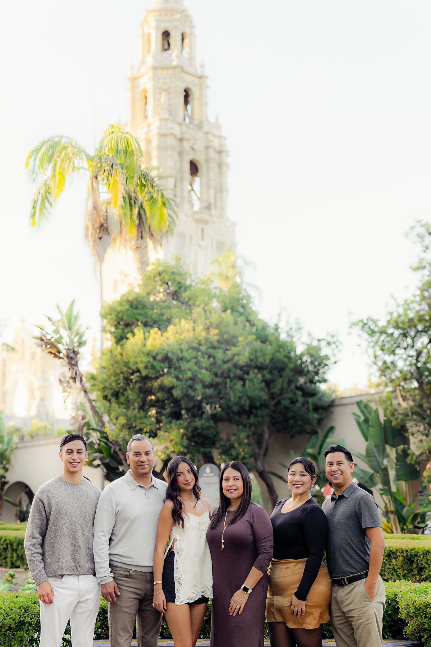 Group portrait against a white Spanish colonial church facade with palm trees and landscaping visible.