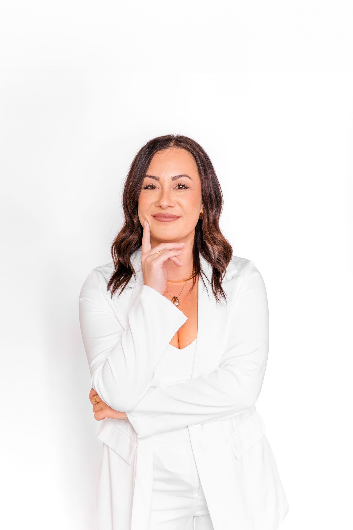 Professional portrait of someone in an all-white business outfit posing confidently against a white background.