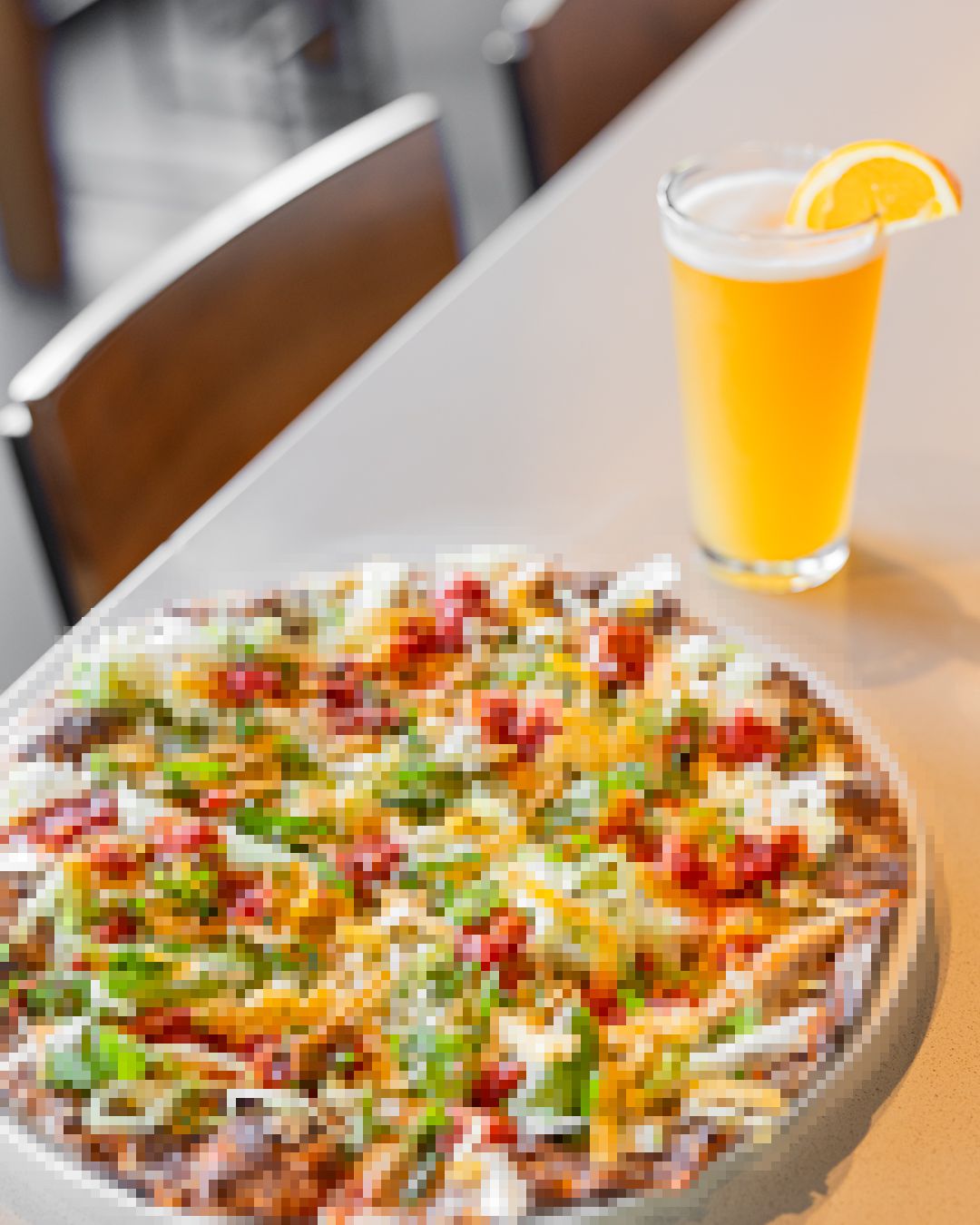 Colorful loaded nachos with toppings and beer served on a restaurant table.