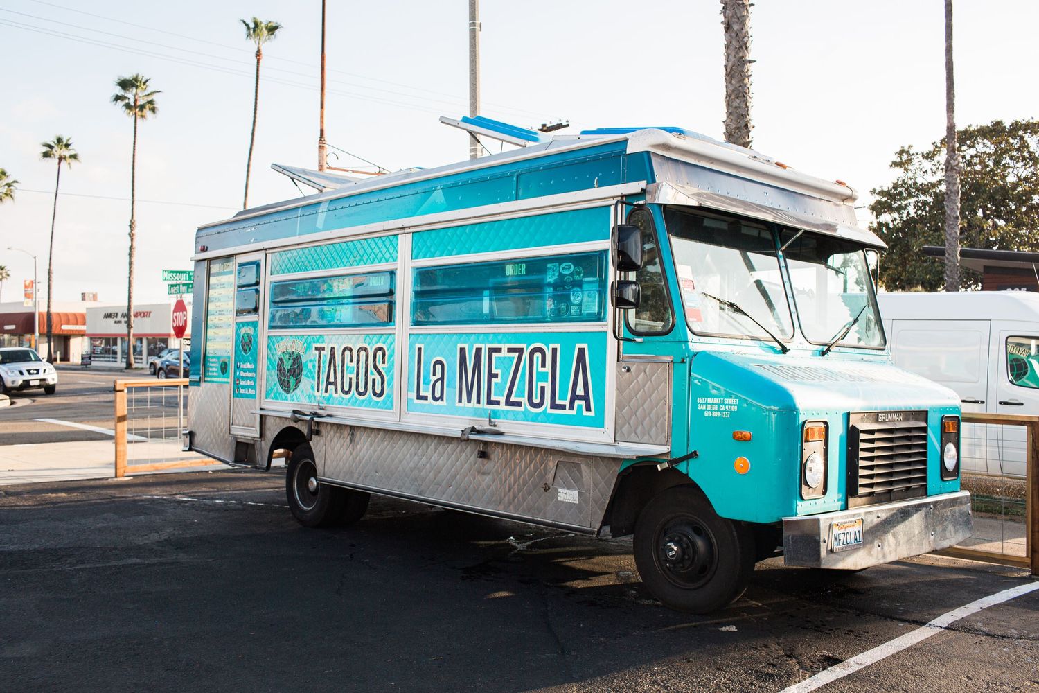 A turquoise and white vintage food truck with retro styling is parked in an outdoor lot during daytime.