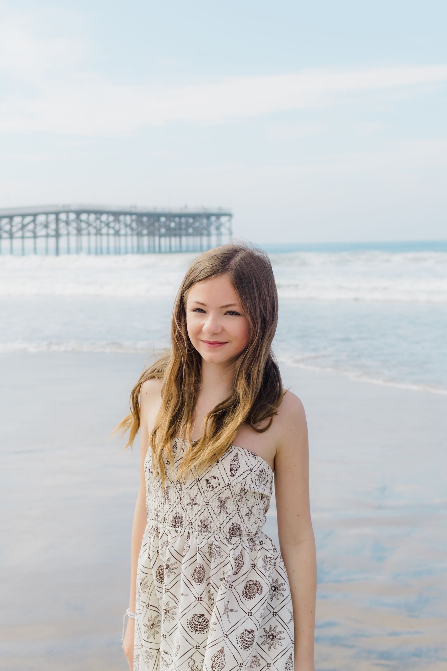Scenic beach photoshoot featuring a lace dress and ocean pier in the background.