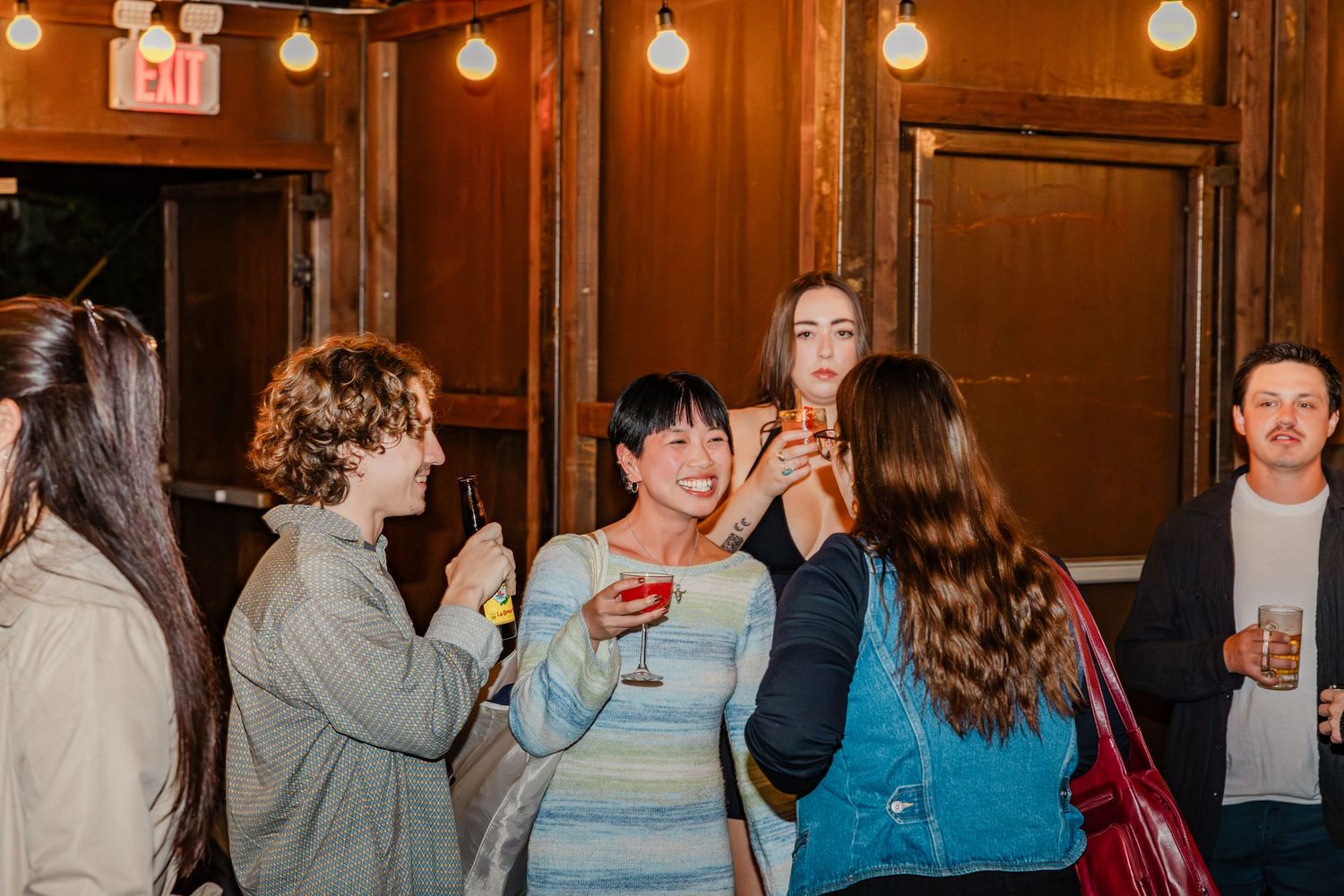 People gathered in a cozy wood-paneled venue with glowing spherical pendant lights creating warm ambiance.