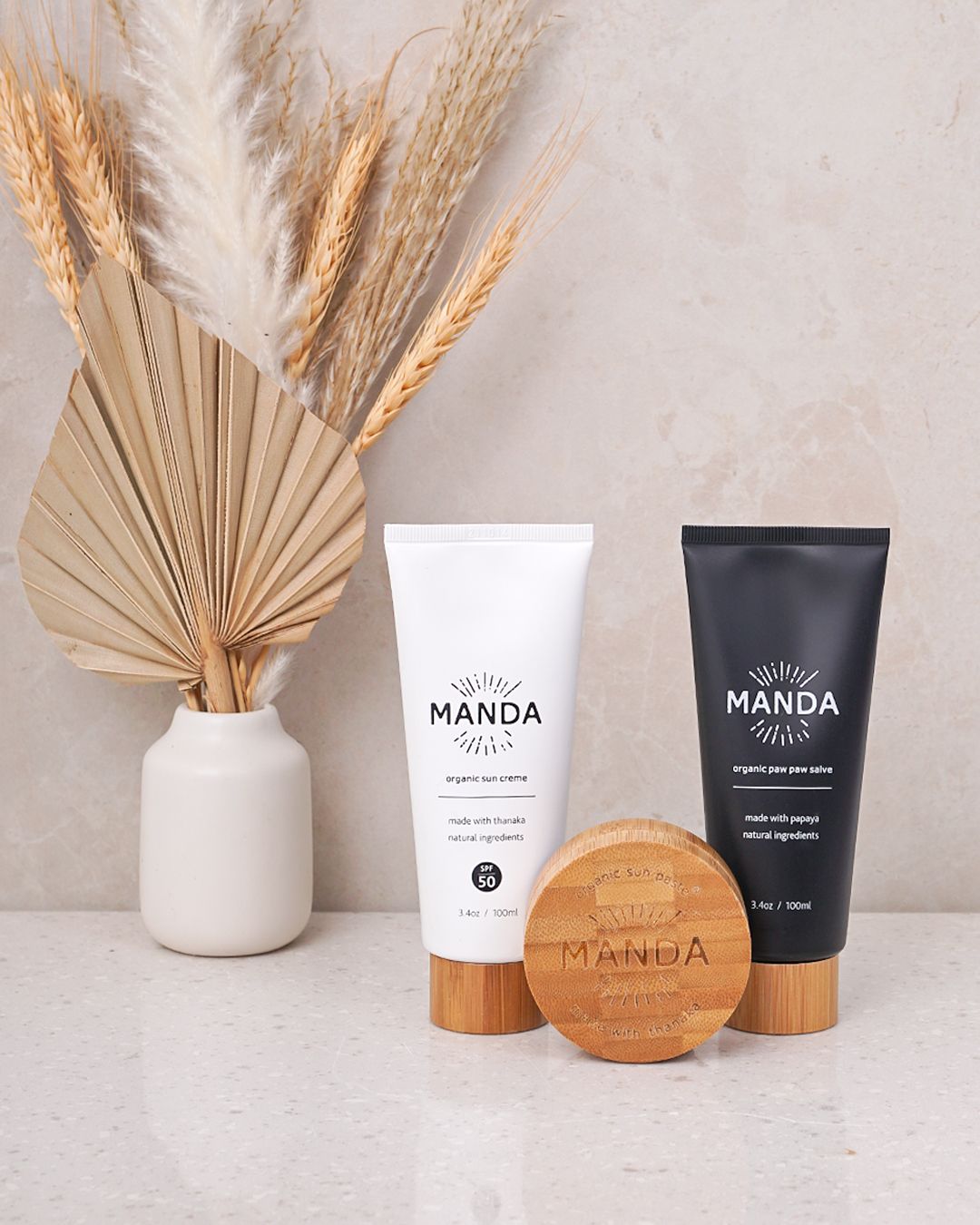 Minimalist beauty product display with dried palm leaves and neutral toned packaging.