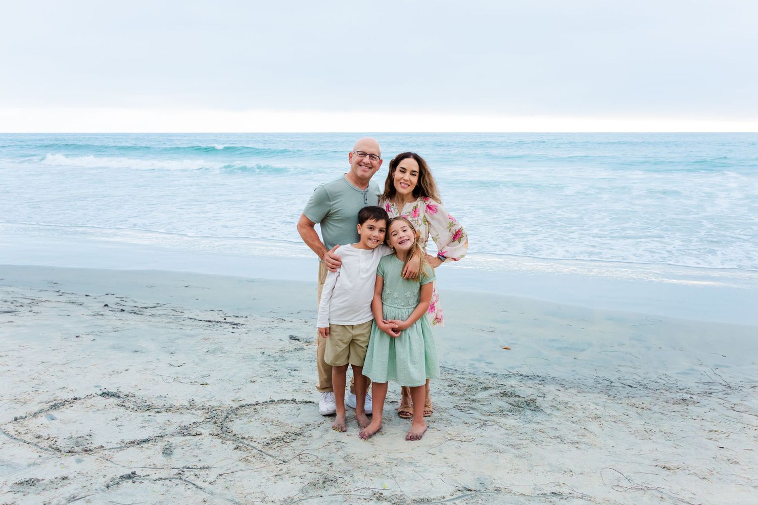 A family group poses for a beach portrait with the ocean waves behind them.