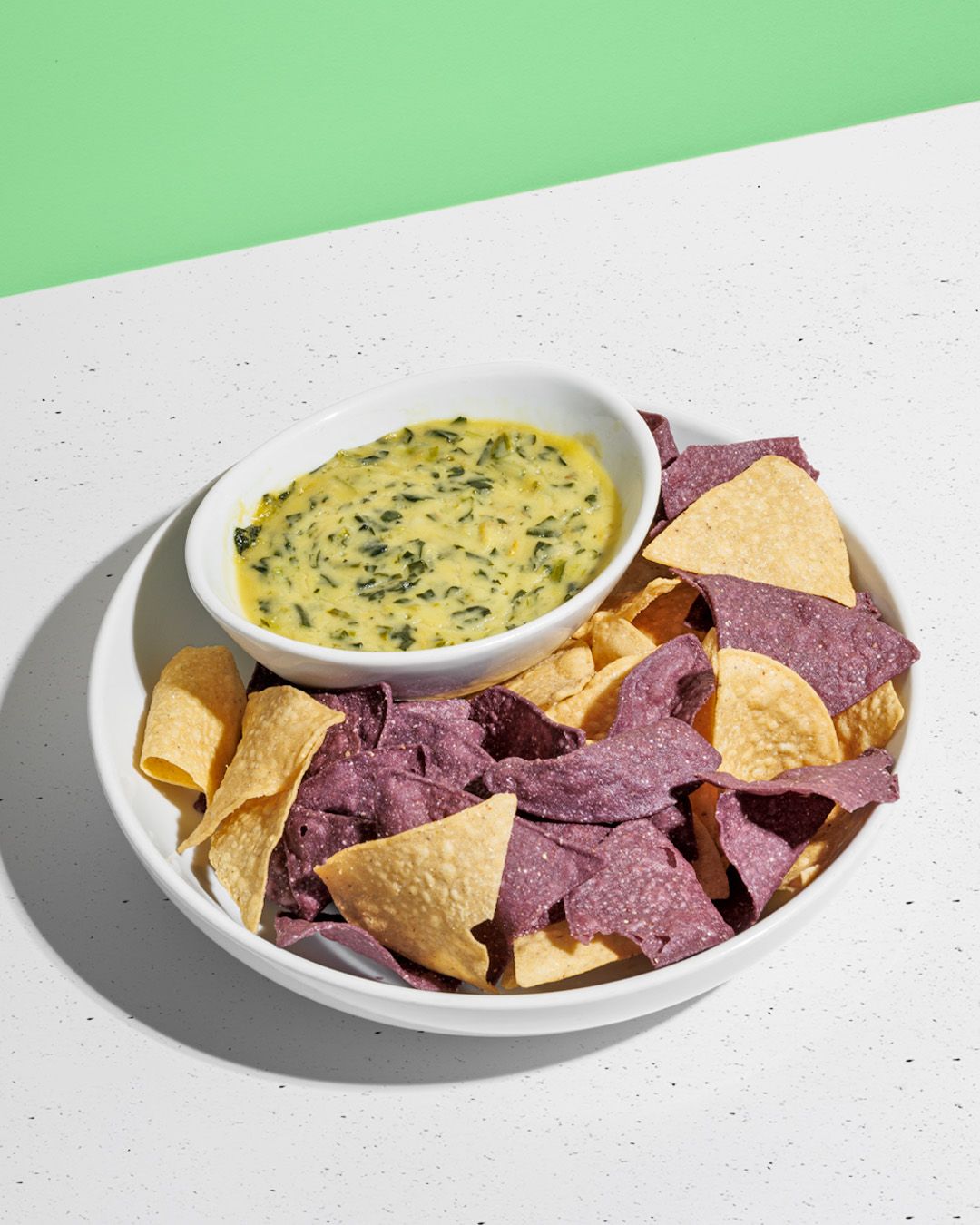 Colorful tortilla chips served with creamy queso dip on white plates.