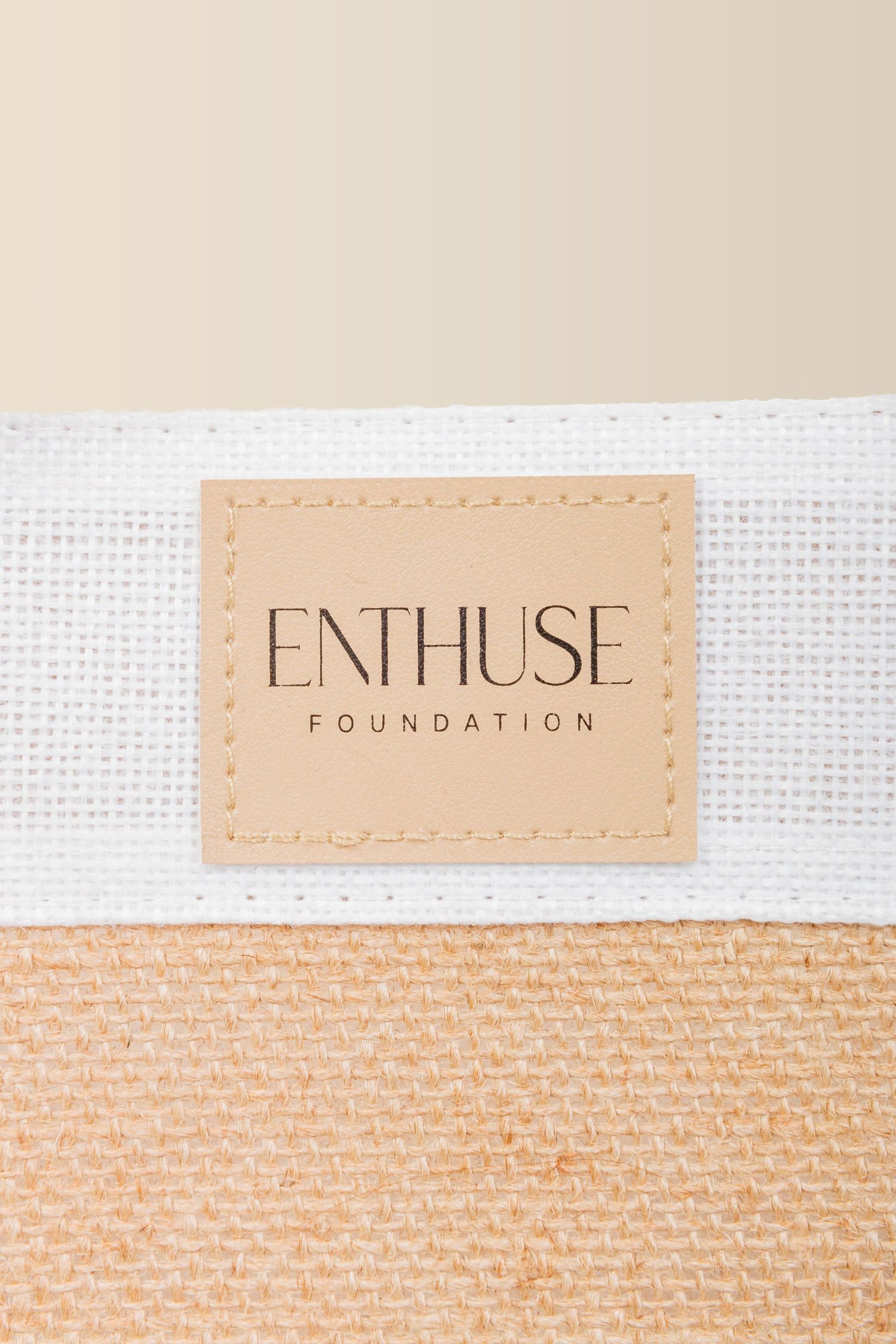 Close-up of a beige leather tag with 'ENTHUSE FOUNDATION' branding on white textile material.