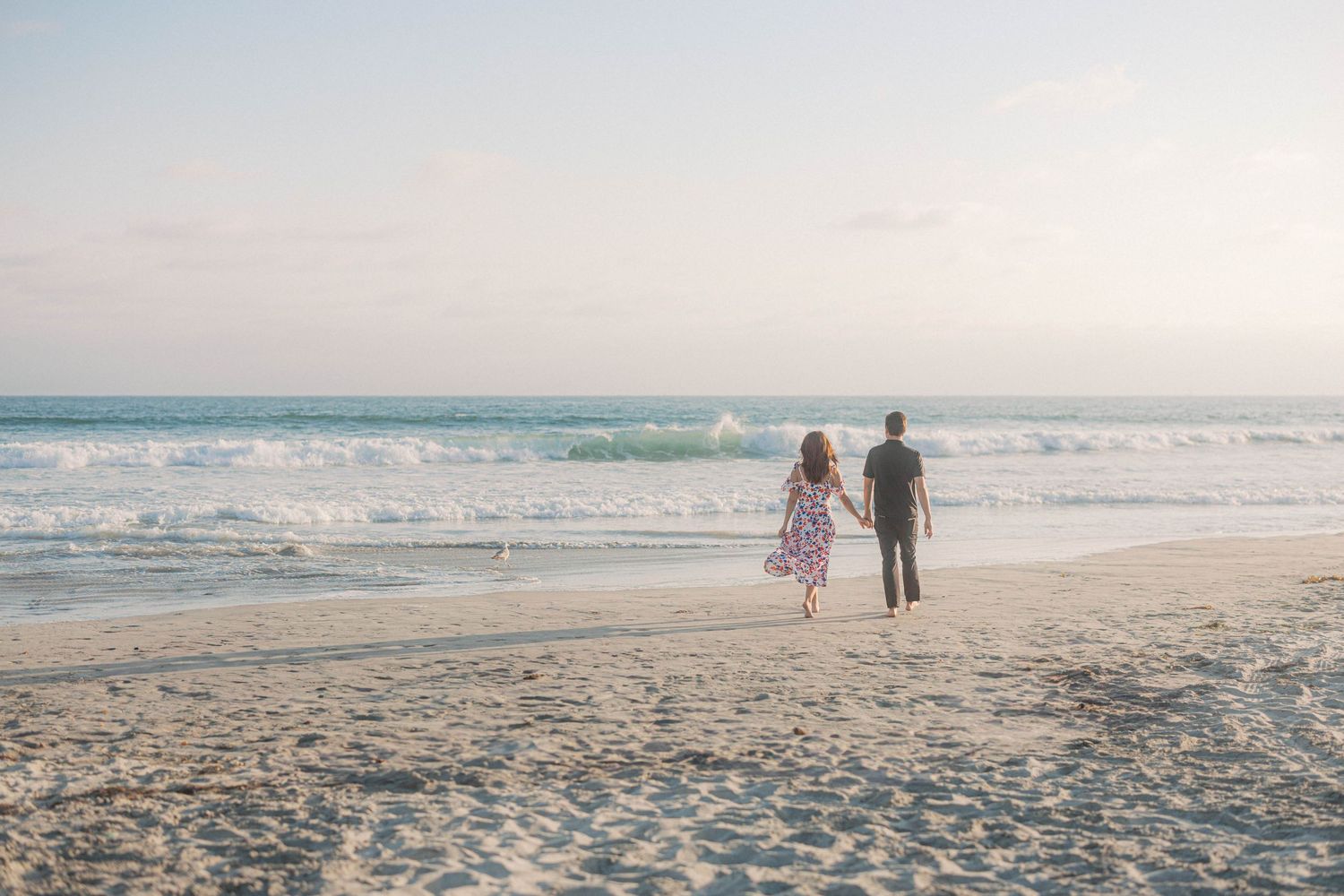 Two people walk together holding hands along a beautiful beach at sunset with waves rolling onto the shore.