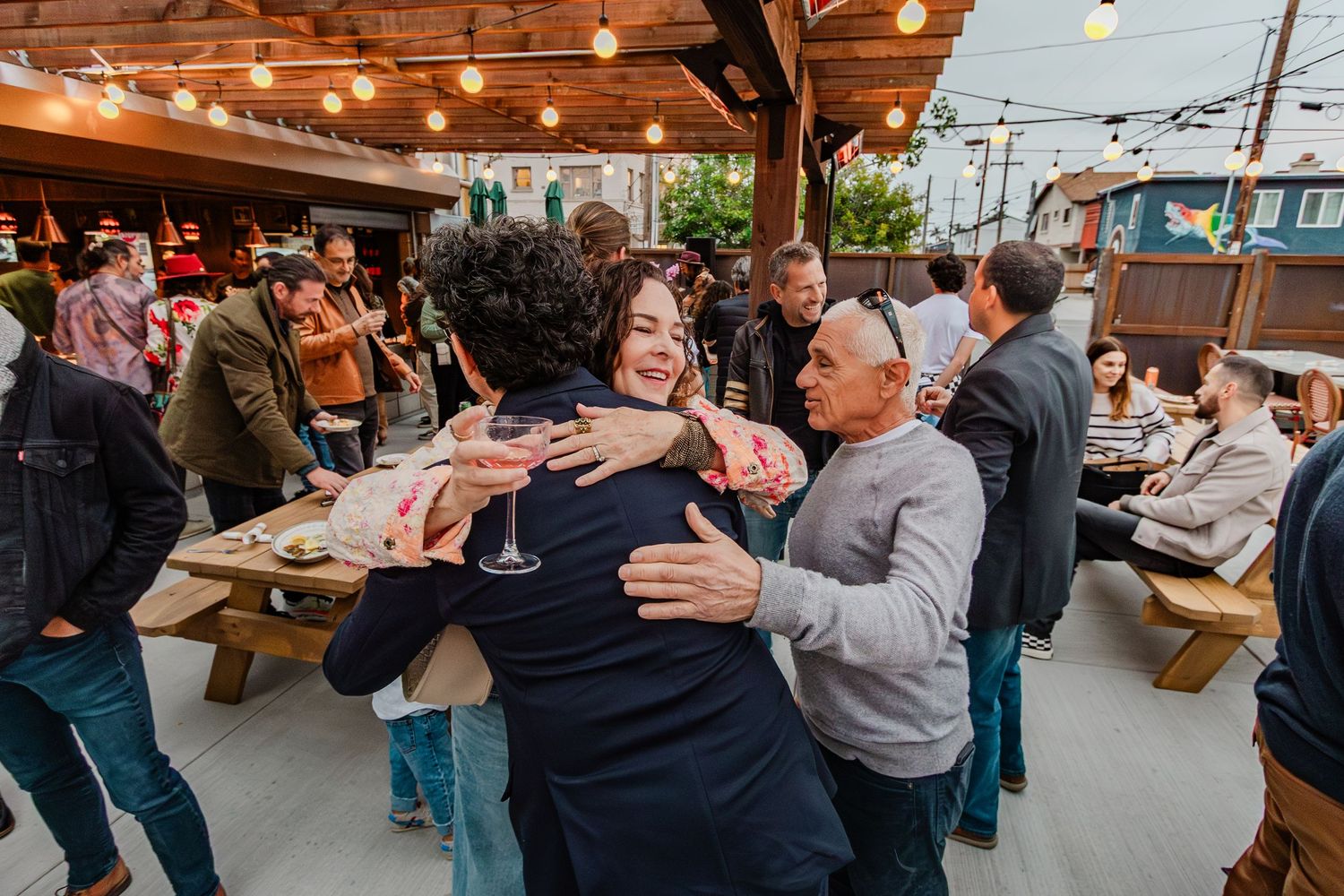 People embracing and celebrating at casual outdoor dining space with string lights.