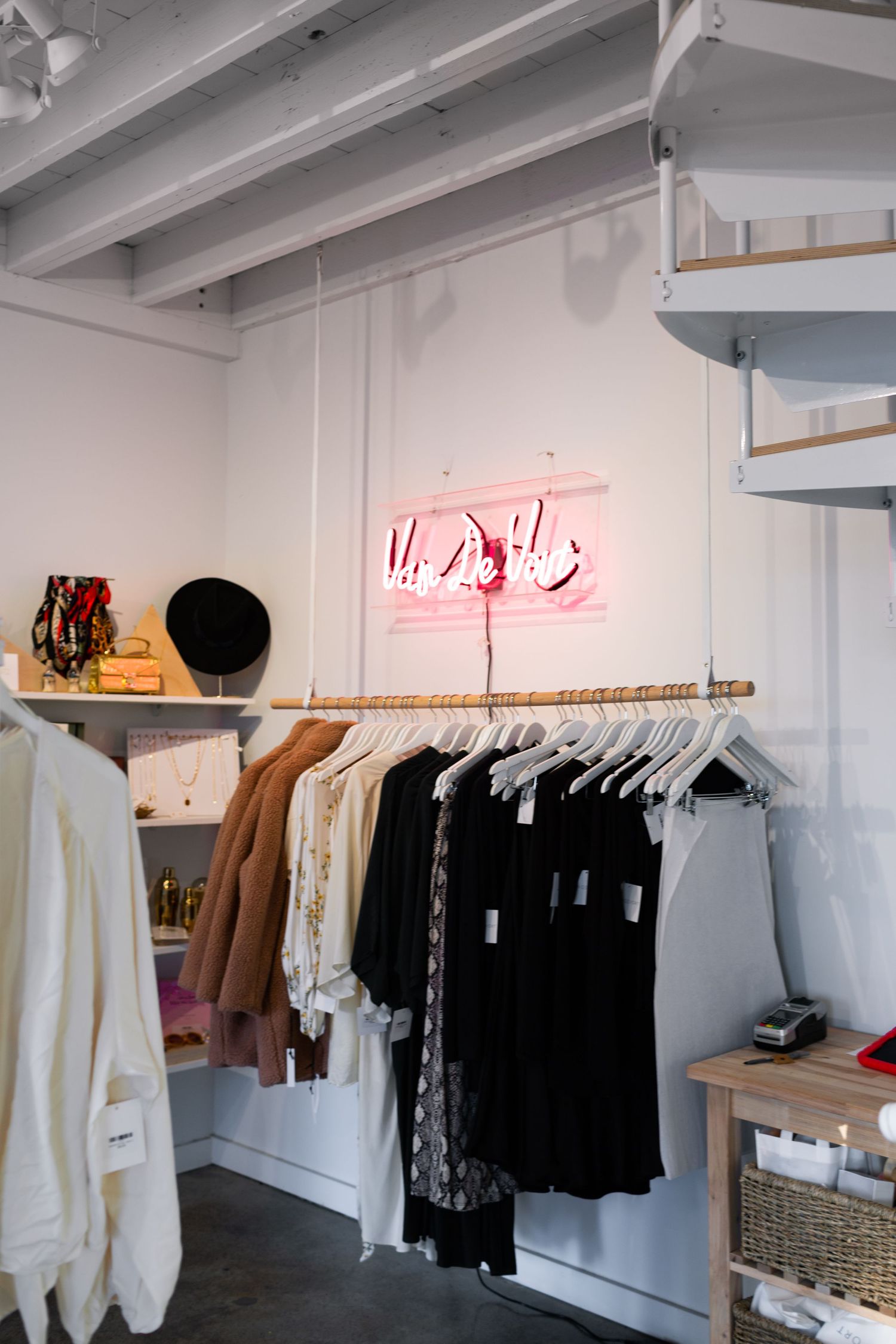 Modern retail clothing store interior with white walls and exposed beams showing racks of black and white garments.