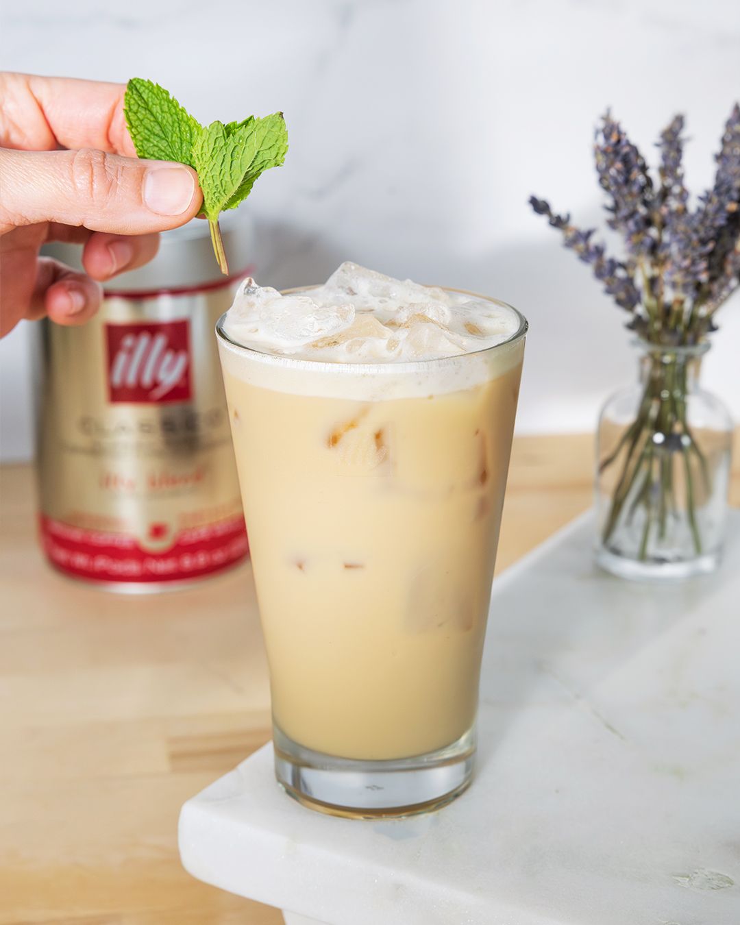 Iced latte topped with whipped cream and fresh mint leaf beside lavender bouquet.