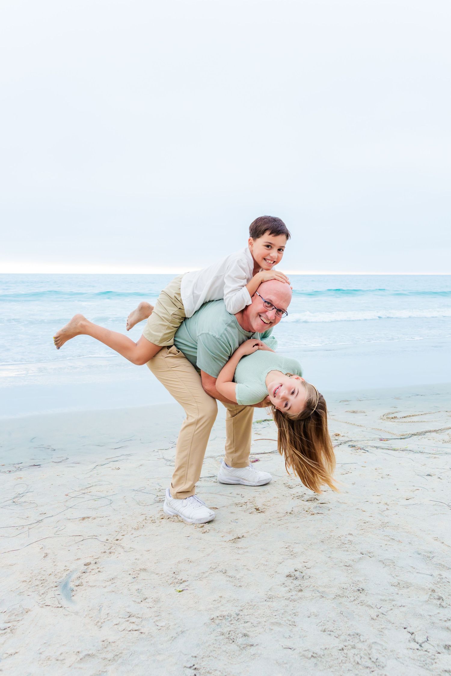 A playful group poses in a fun arrangement on a beach with turquoise ocean waves in the background.