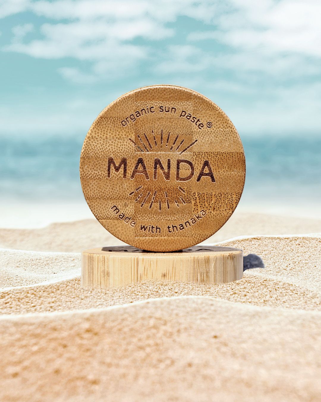 Wooden Manda sun care product photographed in sand with beach backdrop.