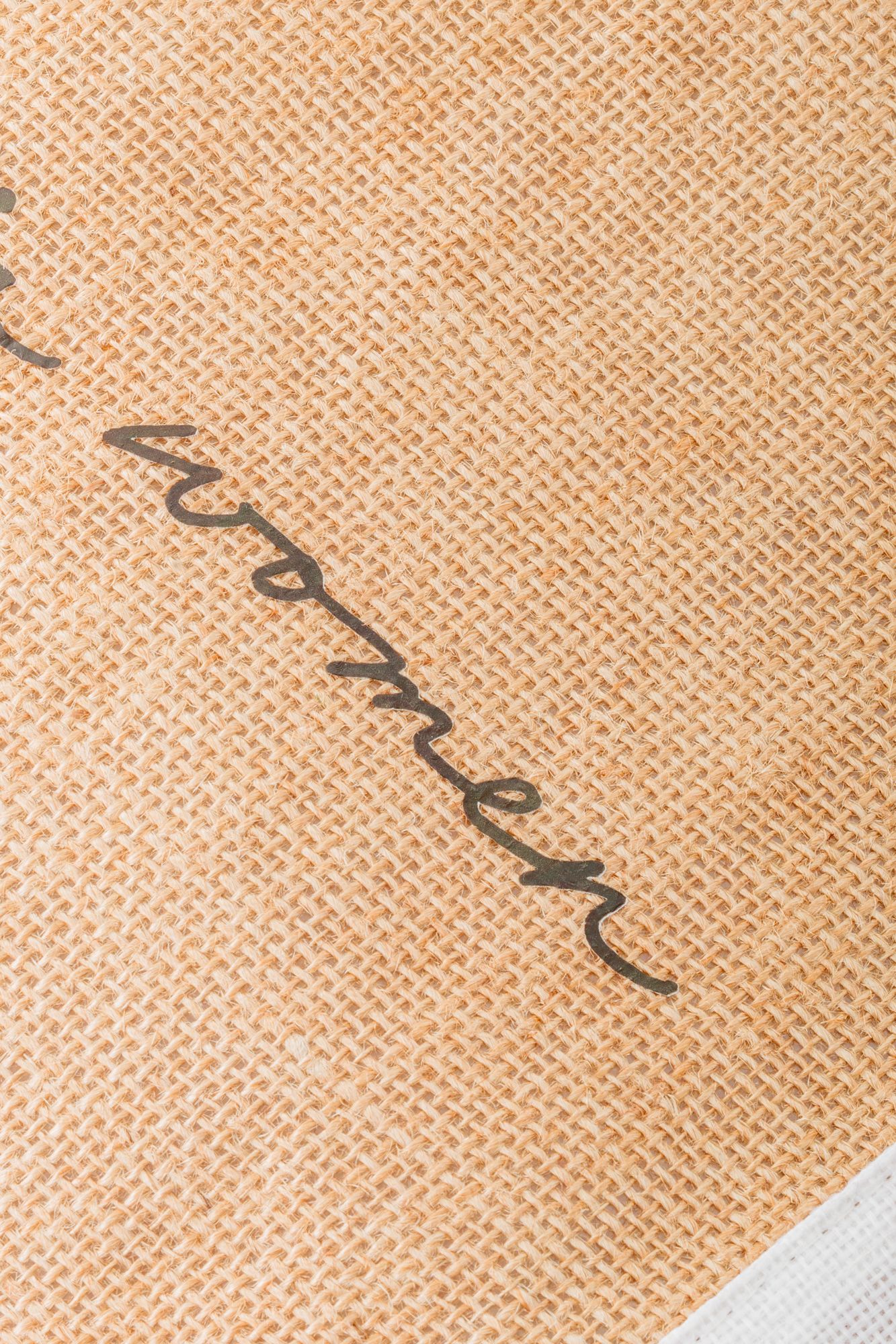 Extreme close-up of cursive text embroidered on tan canvas textile material.