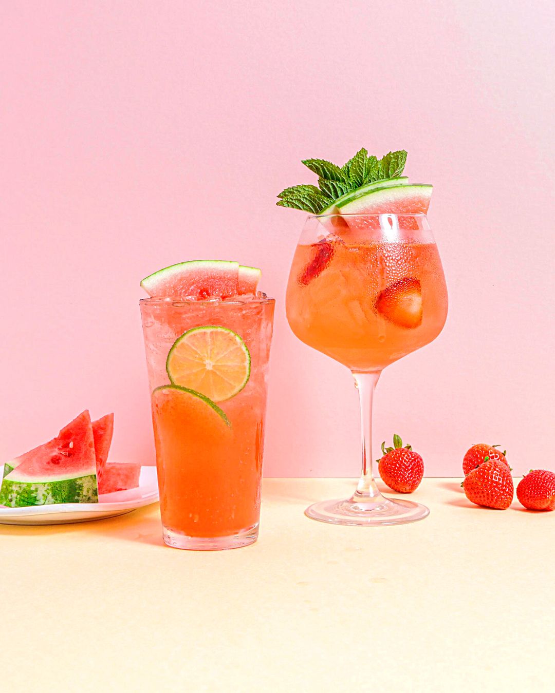 Pink strawberry cocktails with citrus garnishes arranged in glasses.