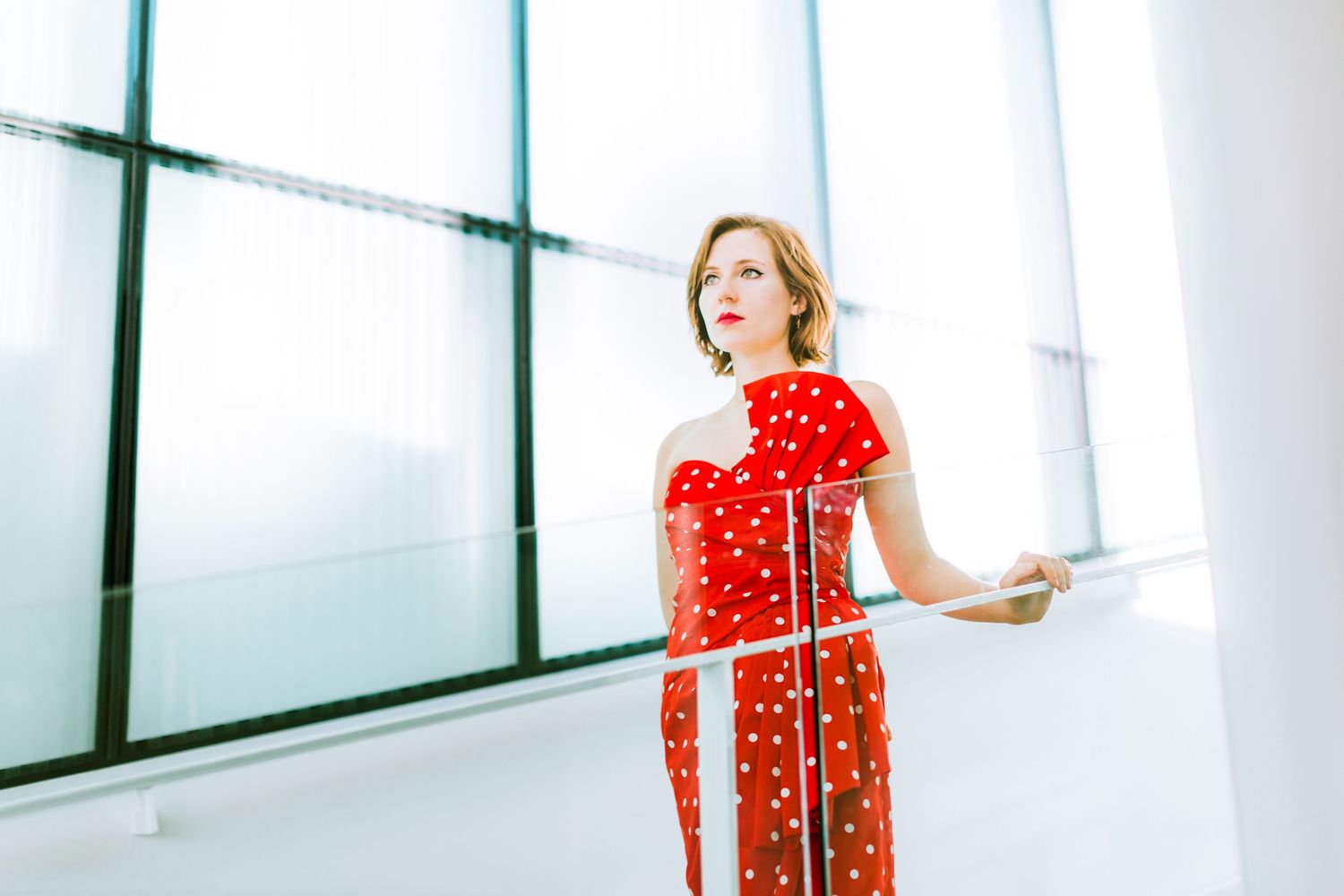 Fashion photos in a modern white interior space wearing a red polka dot dress.