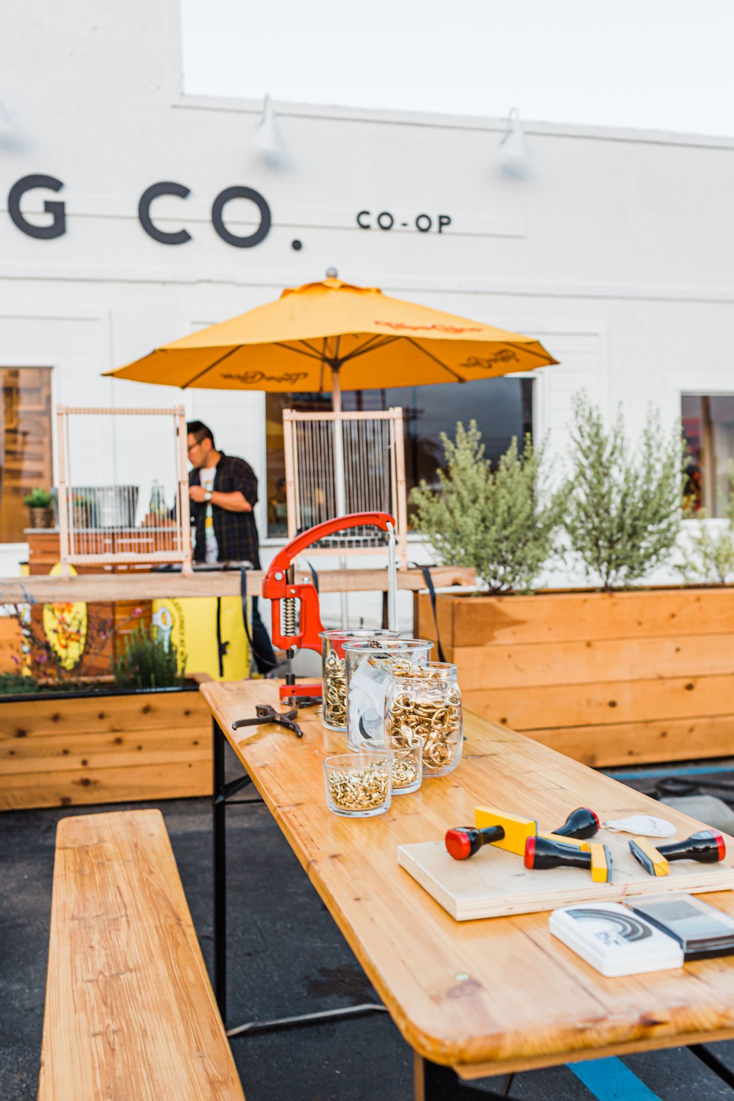 Wooden outdoor dining tables with orange umbrellas at a modern co-op cafe patio.