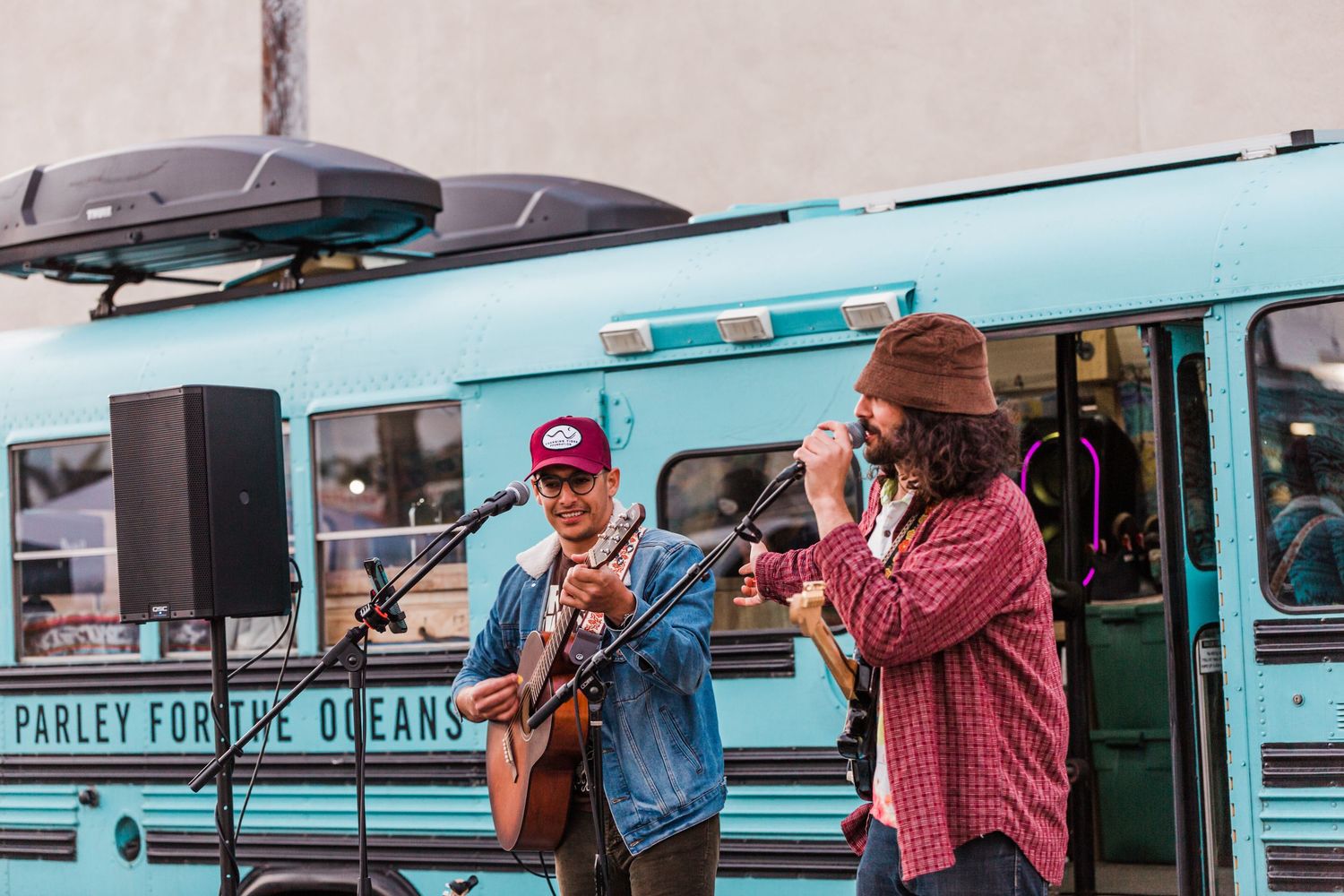 Two musicians performing live music outside a turquoise food truck on a sunny day.