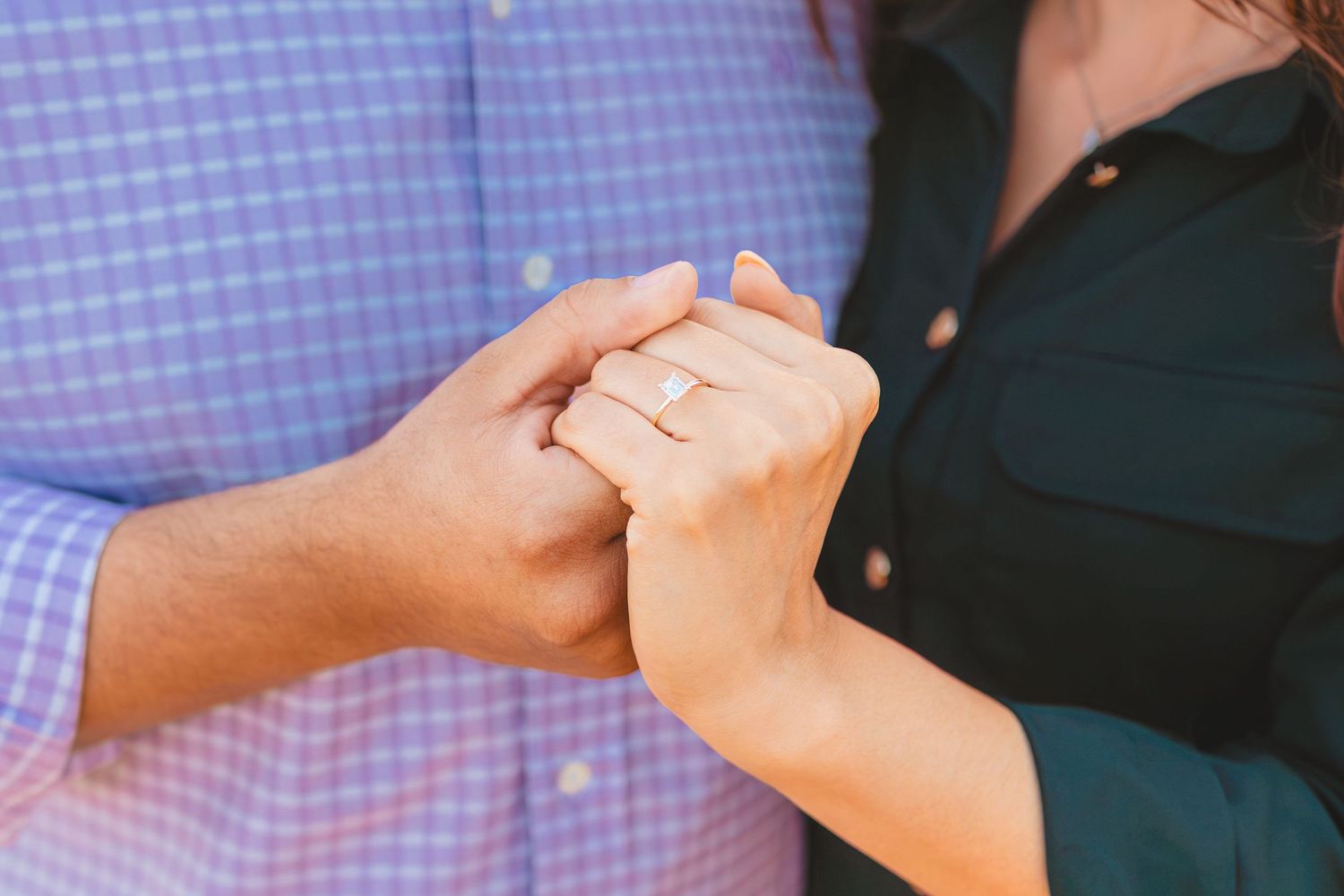 Close up of hands showing off an engagement ring against a blue and white background.