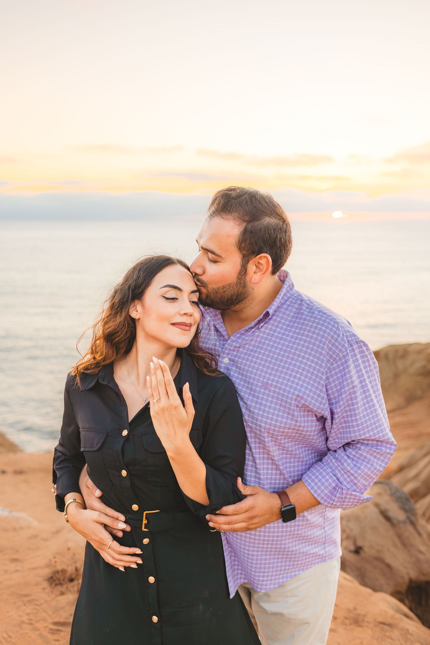 Tender embrace between two people on oceanside cliffs during warm sunset lighting.