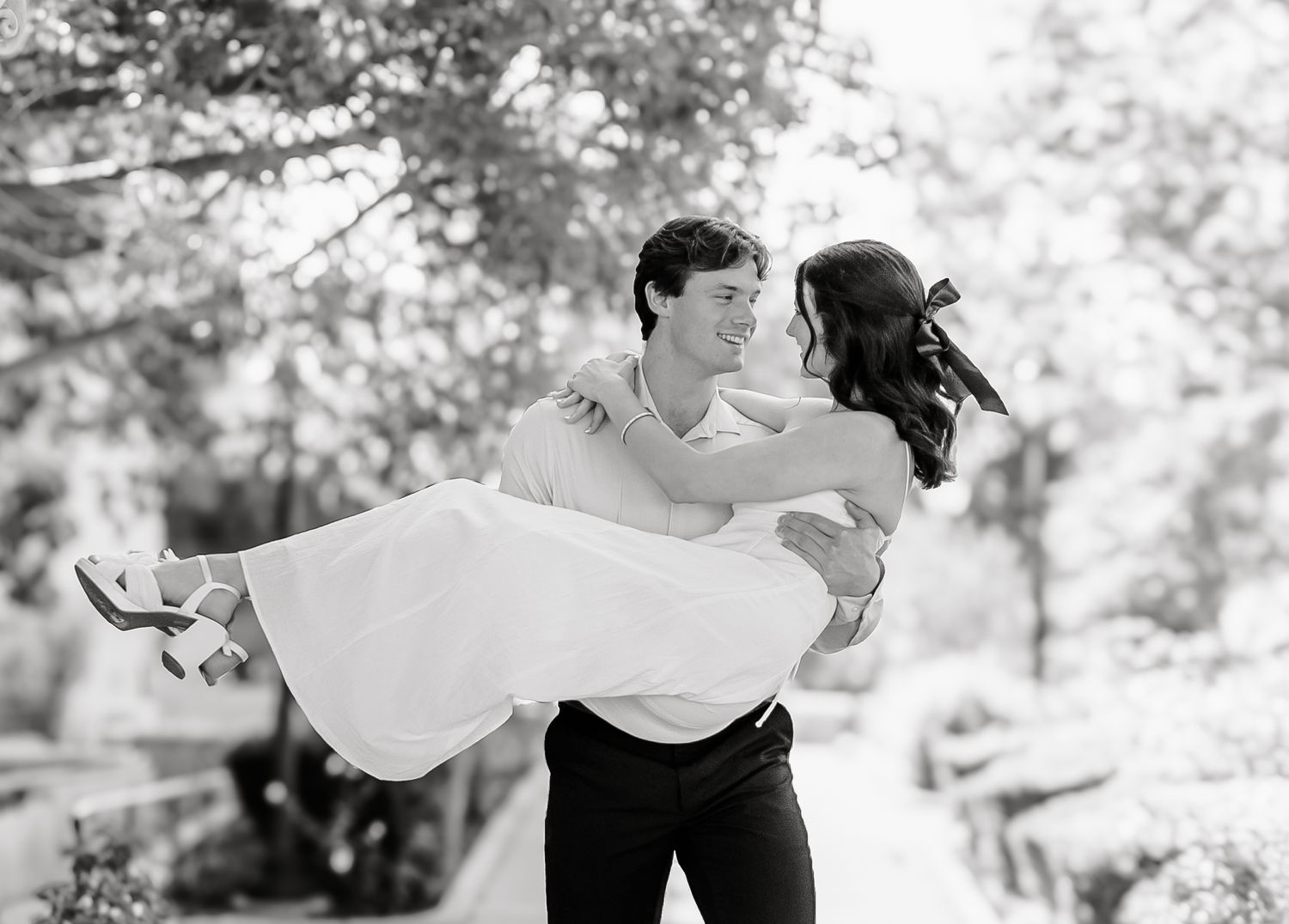 A couple dances gracefully together in a romantic outdoor setting with trees in the background.